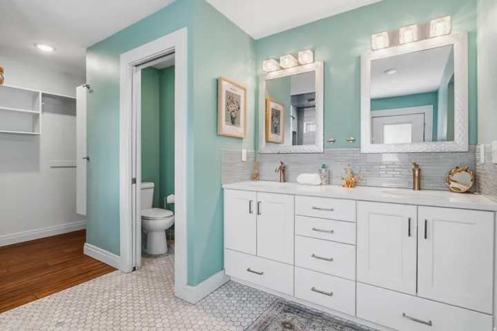 Dual vanity with integrated sinks, white cabinetry, hexagon tile flooring, and a walk-in closet with built-in shelving
