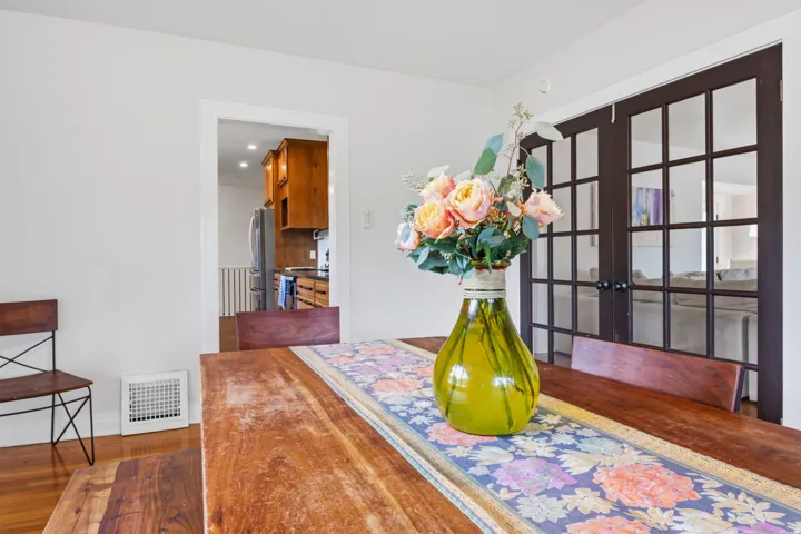 Hardwood flooring, painted walls, white trim, and a doorway to the kitchen with wood cabinetry and a stainless steel refrigerator
