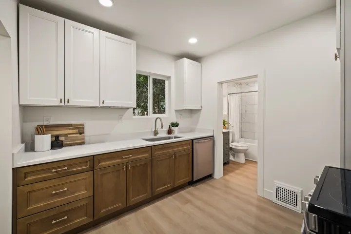 Kitchen featuring a stainless steel dishwasher, white upper cabinetry, wood-finish lower cabinetry, and light-colored countertops