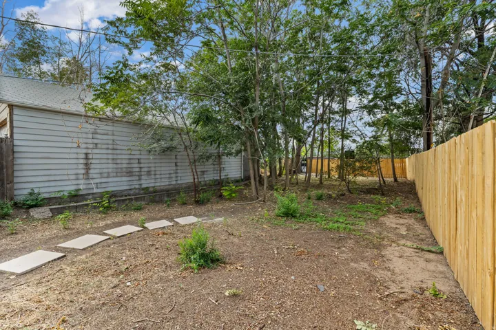 Outdoor space featuring a newly installed privacy fence, mature trees, and stepping stone pathway
