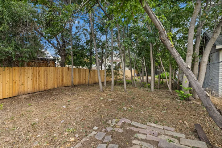 Expansive yard featuring a wooden privacy fence, mature trees, and stone pavers