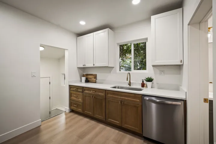 Two-tone cabinetry with white upper cabinets and wood-finish lower cabinets, stainless steel sink with a gooseneck faucet, light-toned countertops, and wood-finish flooring