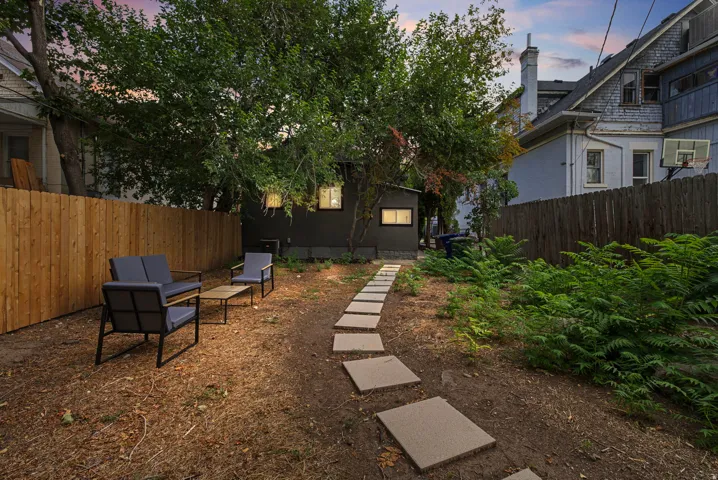 Enclosed backyard featuring a new wood fence, mature trees, garden beds, and stepping stone pathway