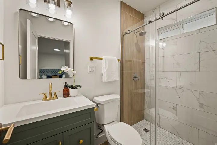 Modern bathroom featuring a vanity with a white countertop and gold-finish faucet, a glass-enclosed shower with a rainfall showerhead, and subway-style wall tiling