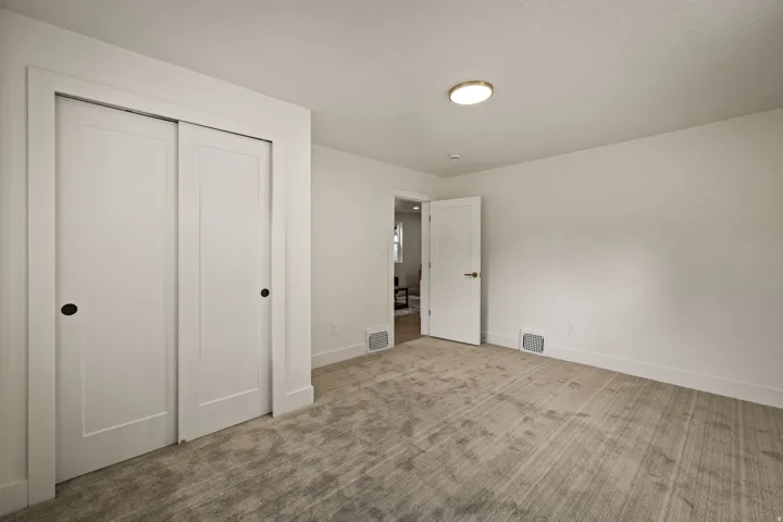 Plush carpeting, bright white walls, modern flush mount ceiling light, and white sliding closet doors with black hardware