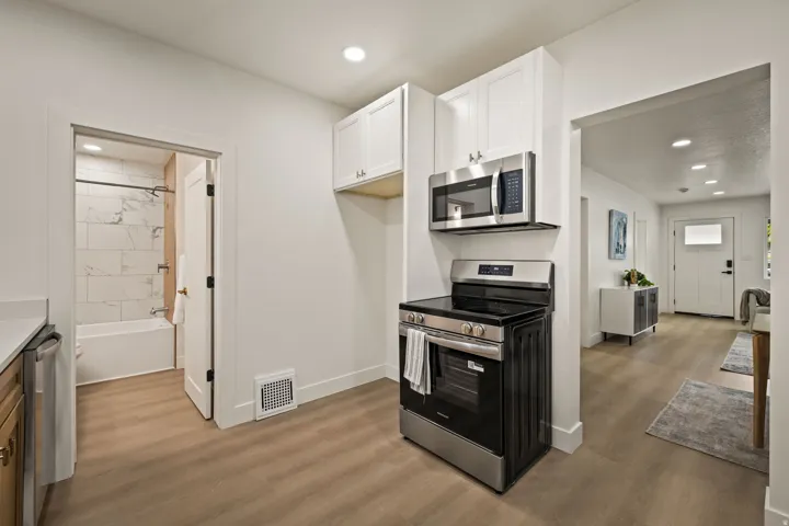 Kitchen featuring stainless steel appliances, white cabinetry, and wood-finish flooring