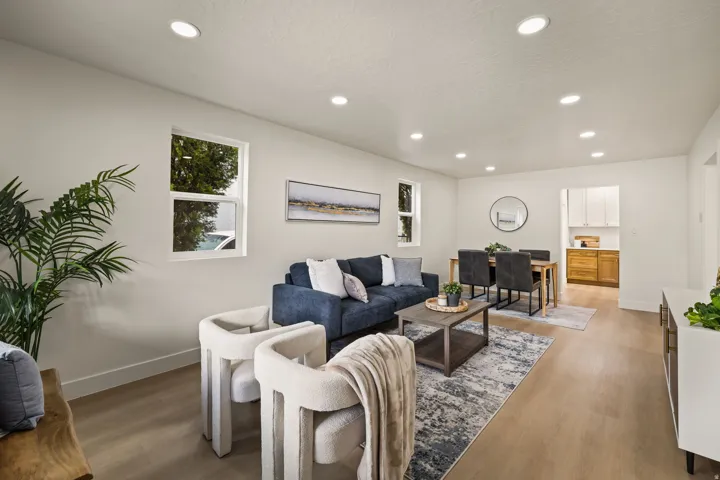 Recessed ceiling lighting, light wood-finish flooring, white walls, two visible windows, and a dining area