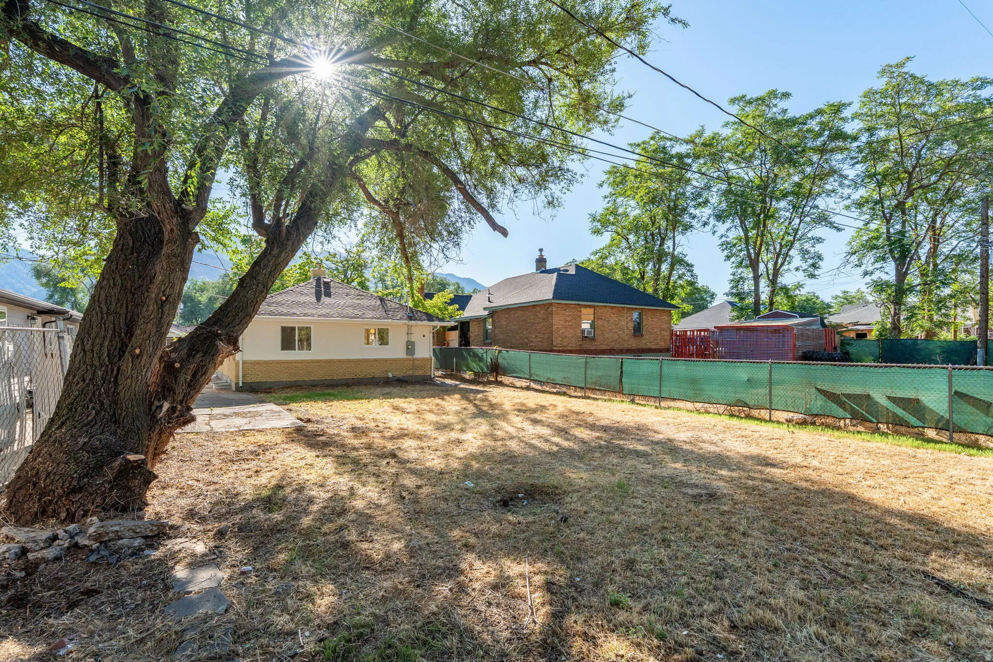 Expansive yard with mature tree, partial chain-link fencing, and mountain backdrop
