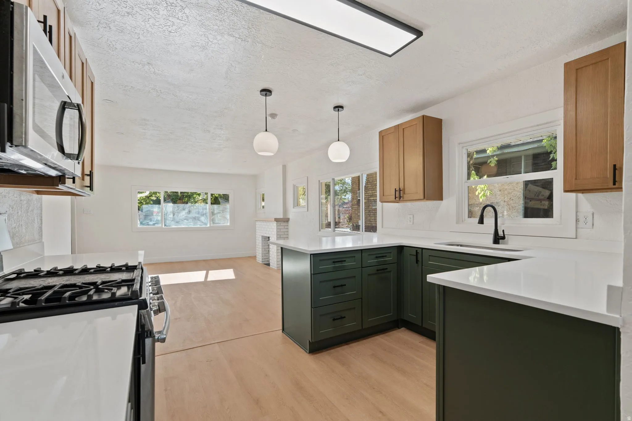 Open-concept kitchen with white countertops, green and wood-finish cabinetry, stainless steel appliances, and wood-finish flooring