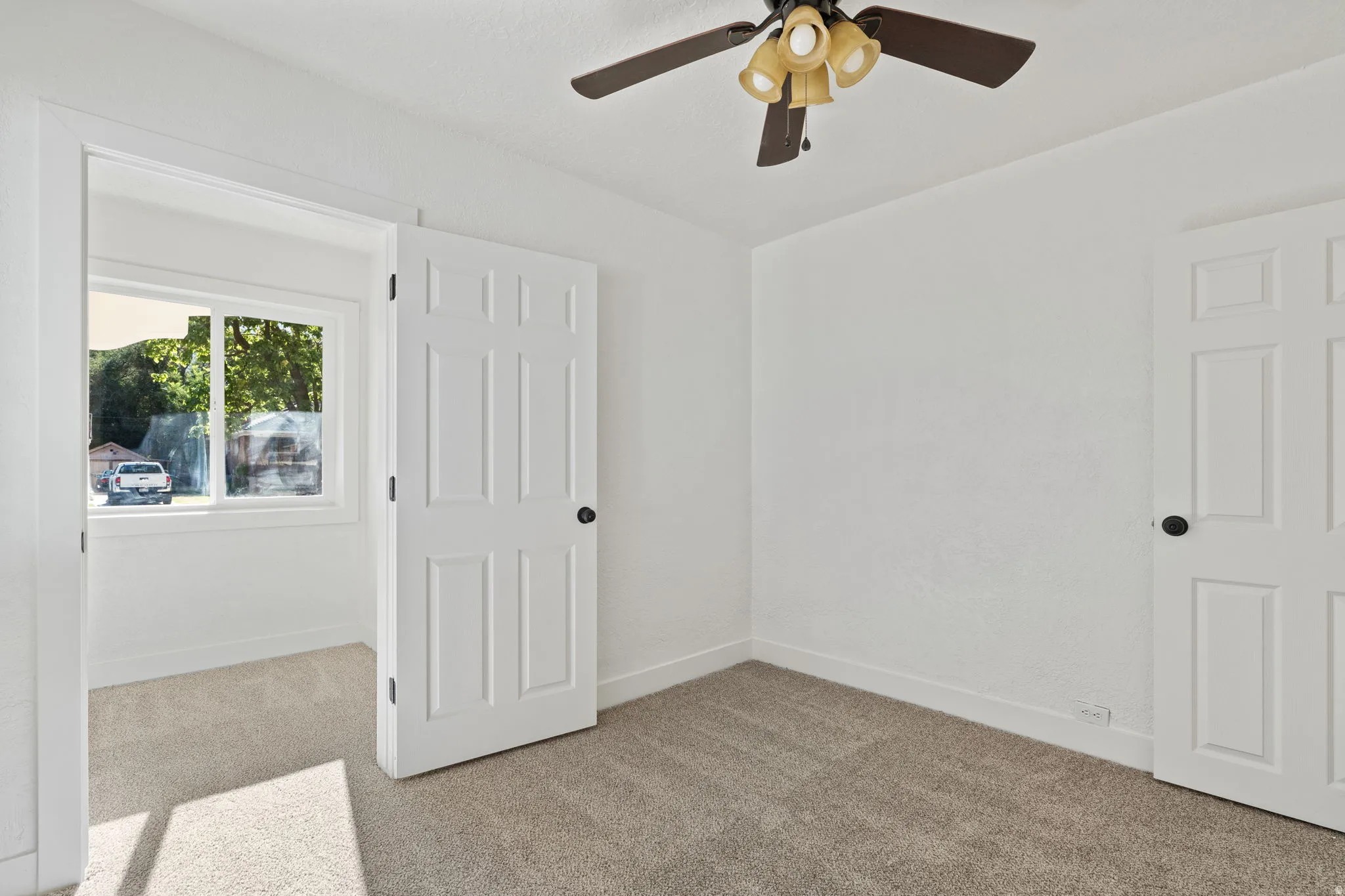Neutral-toned carpeting, white interior doors with black hardware, and a ceiling fan with integrated lighting
