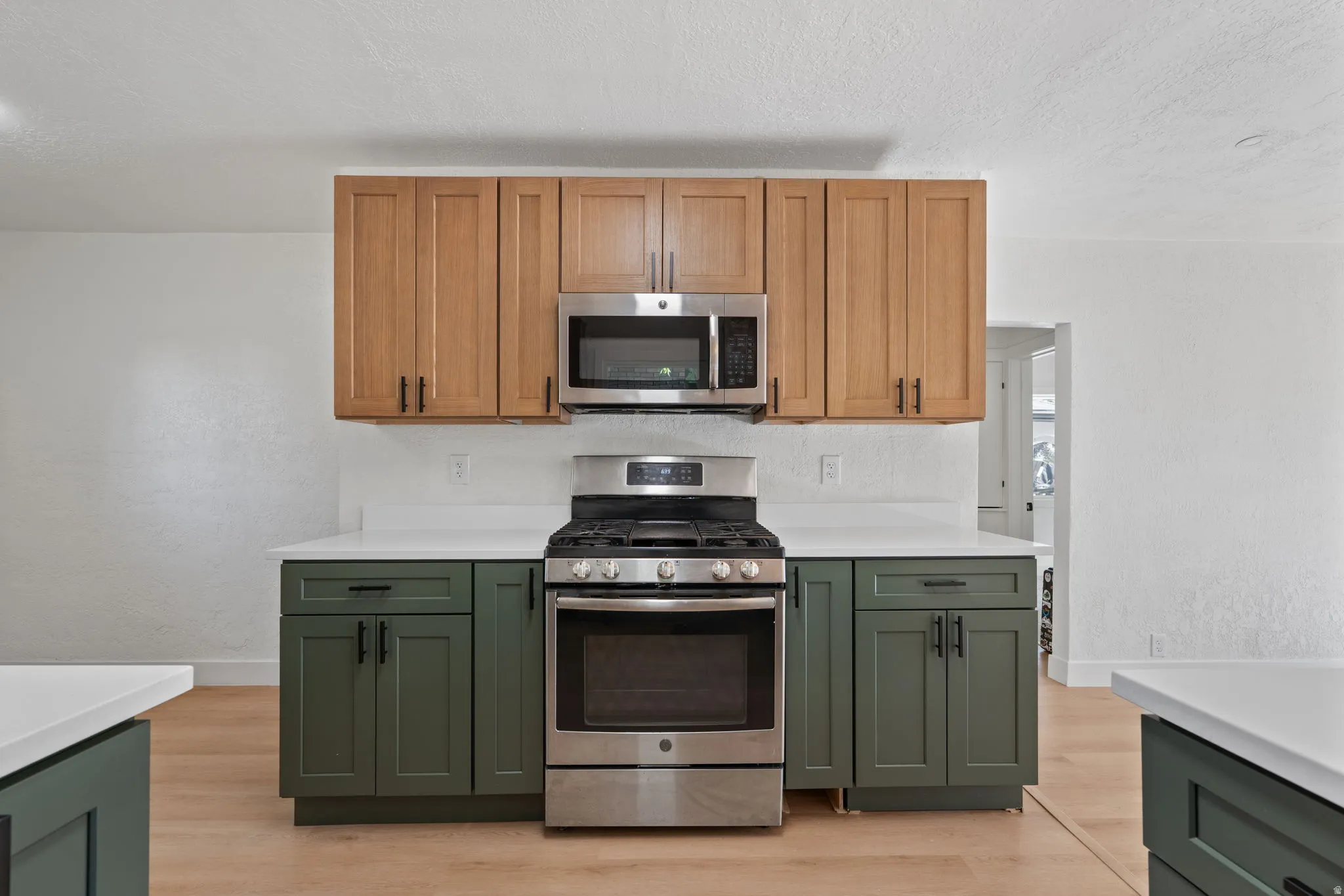 Two-tone cabinetry with stainless steel appliances, white countertops, and wood-finish flooring