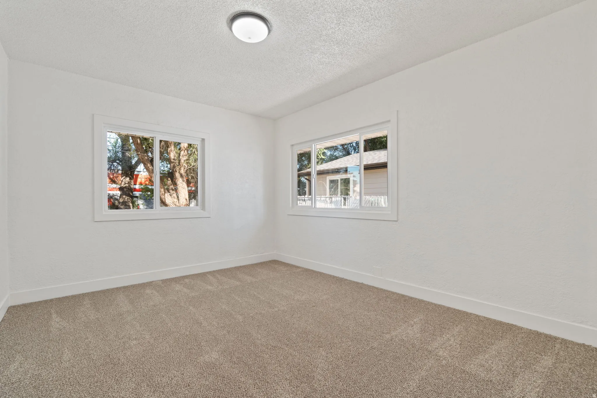 Neutral-toned carpeting, white painted walls, and two windows with white trim, featuring a flush mount ceiling light fixture