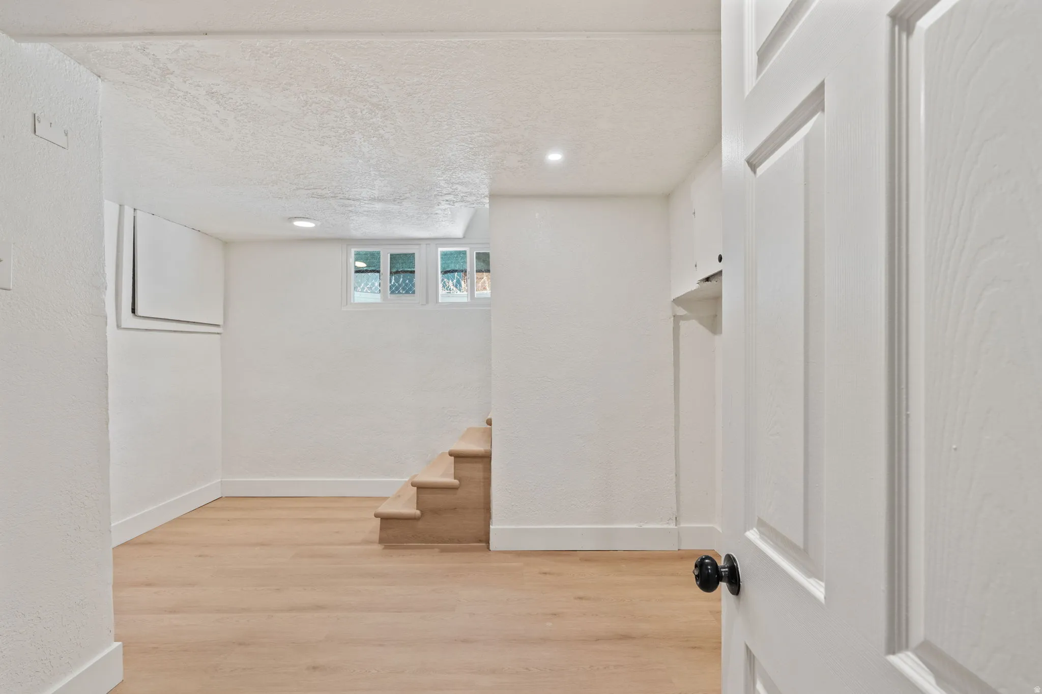 Recessed lighting, wood-finish flooring, white paneled door, black doorknob, and natural light from transom windows