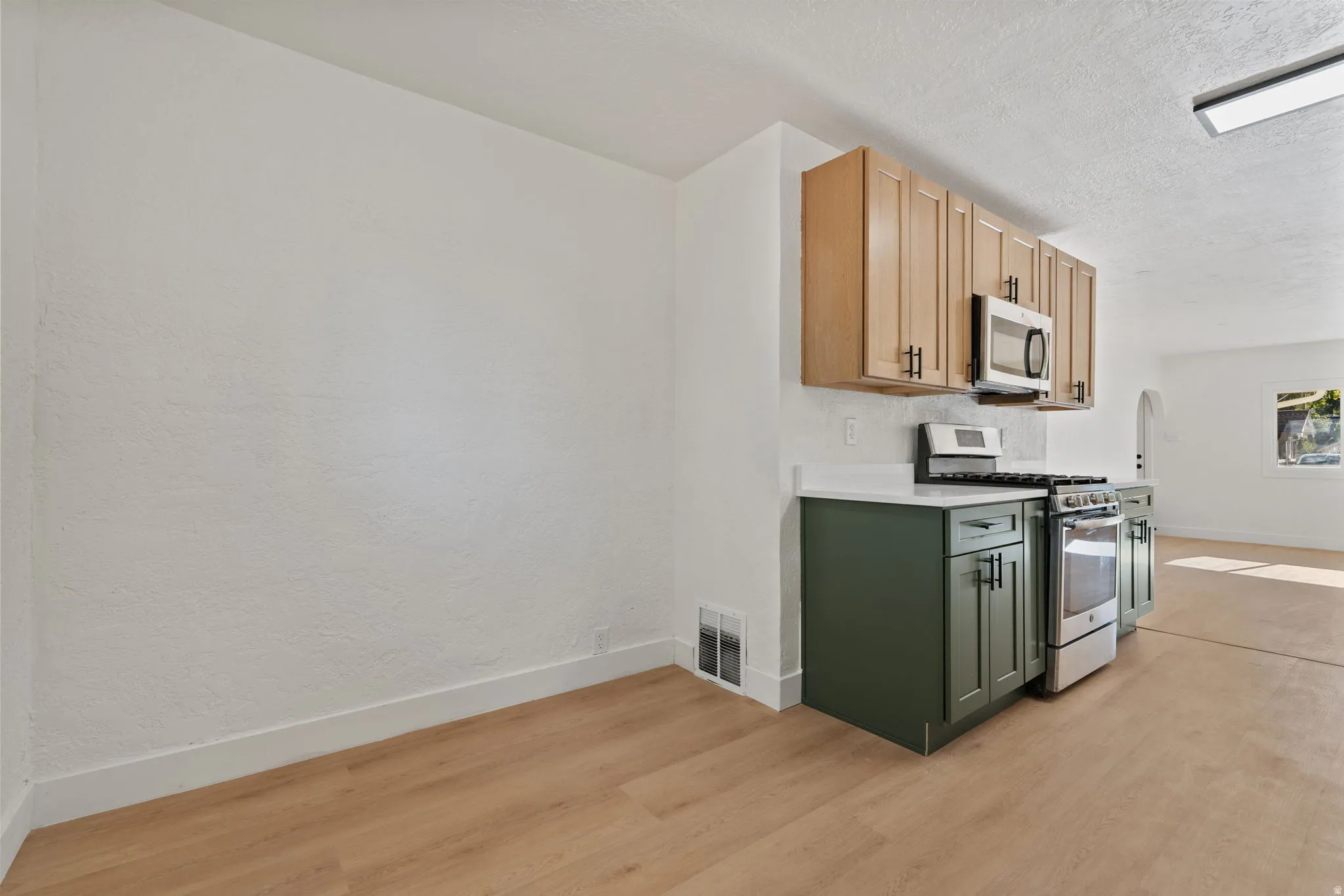Wood-finish flooring, two-tone cabinetry, stainless steel appliances, and white countertops