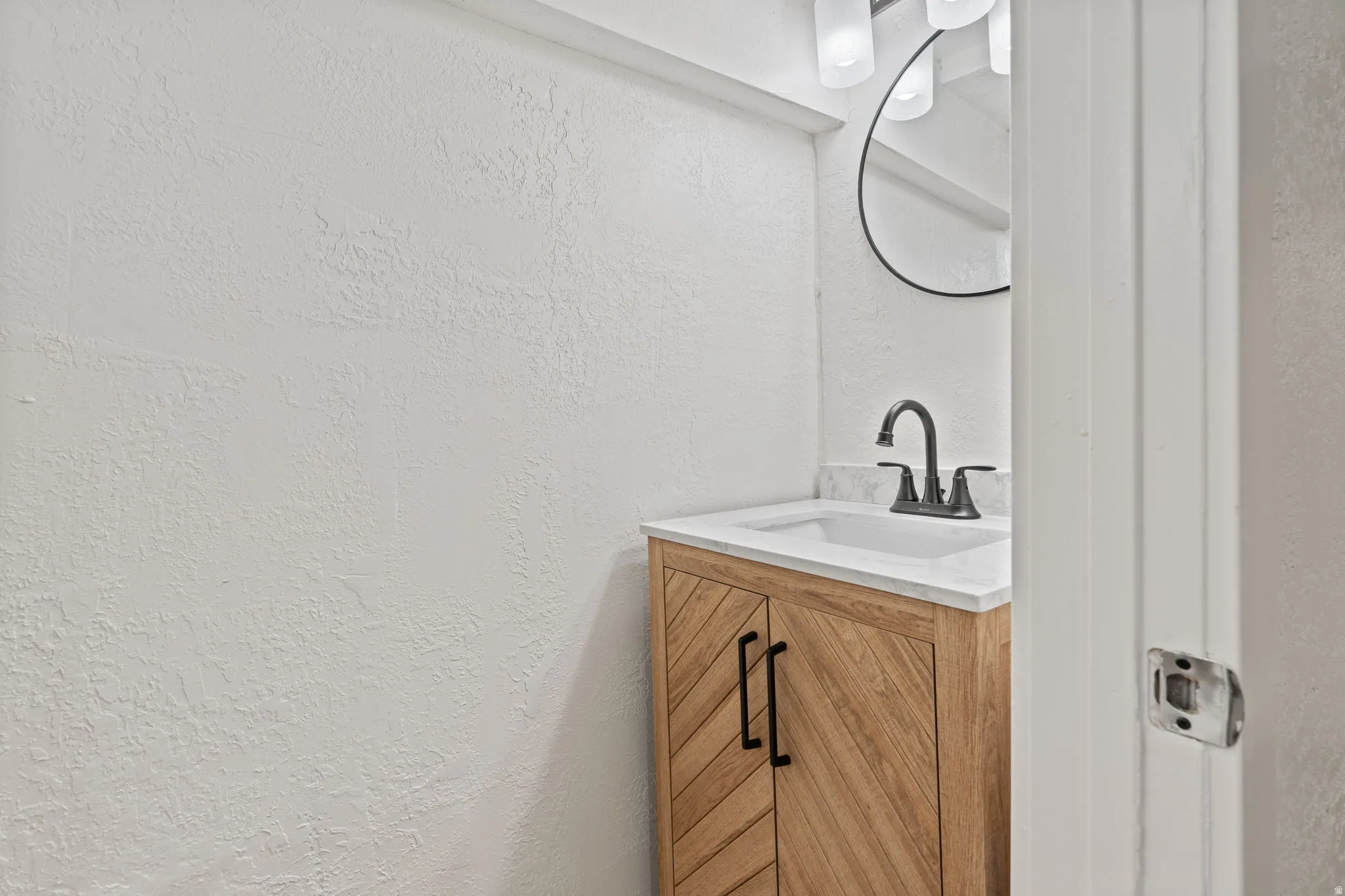 Wood-finish vanity with chevron pattern doors, white countertop, integrated sink, and matte black faucet