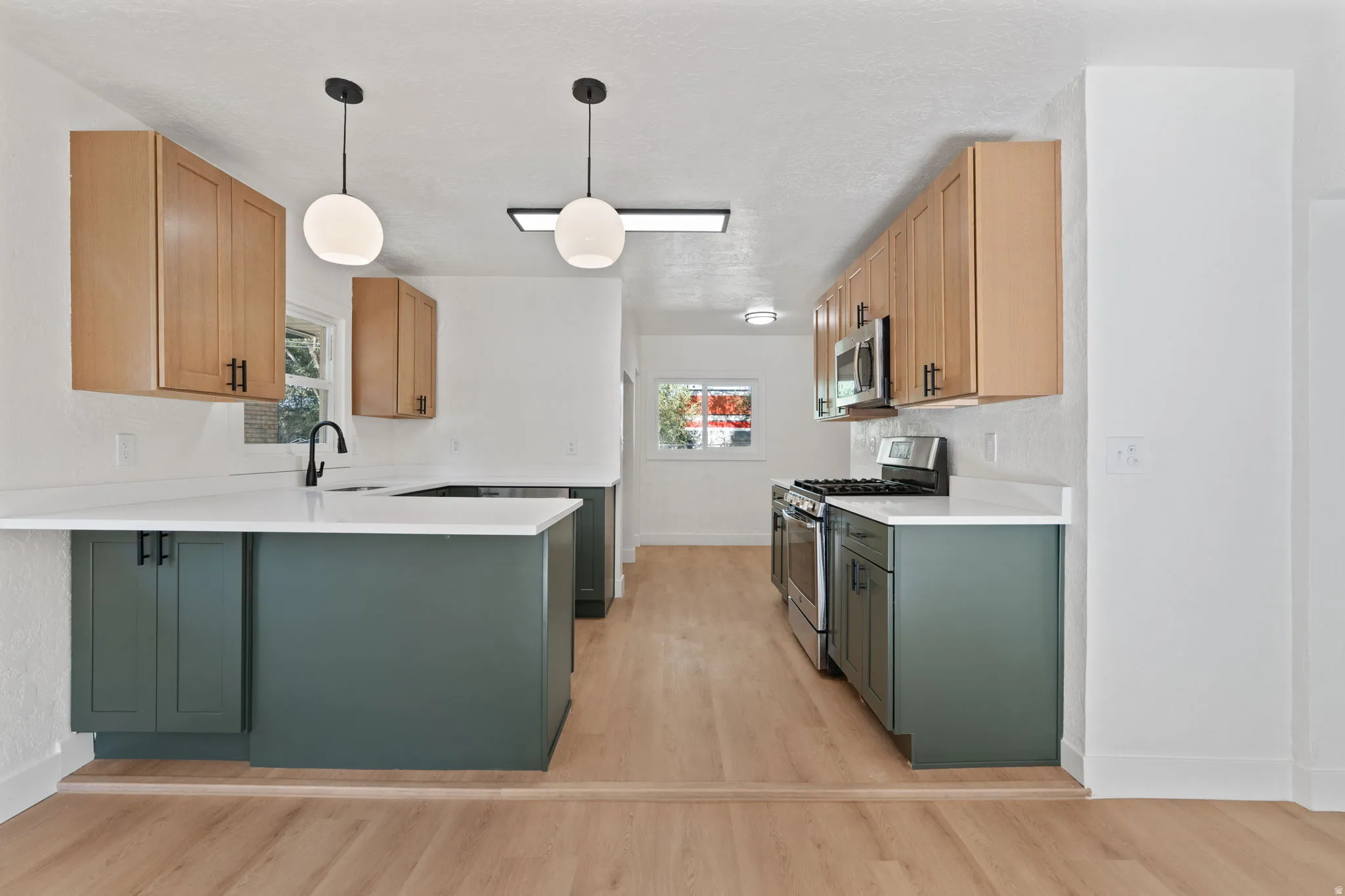 Kitchen featuring wood-finish flooring, two-tone cabinetry, white countertops, black hardware, and stainless steel appliances