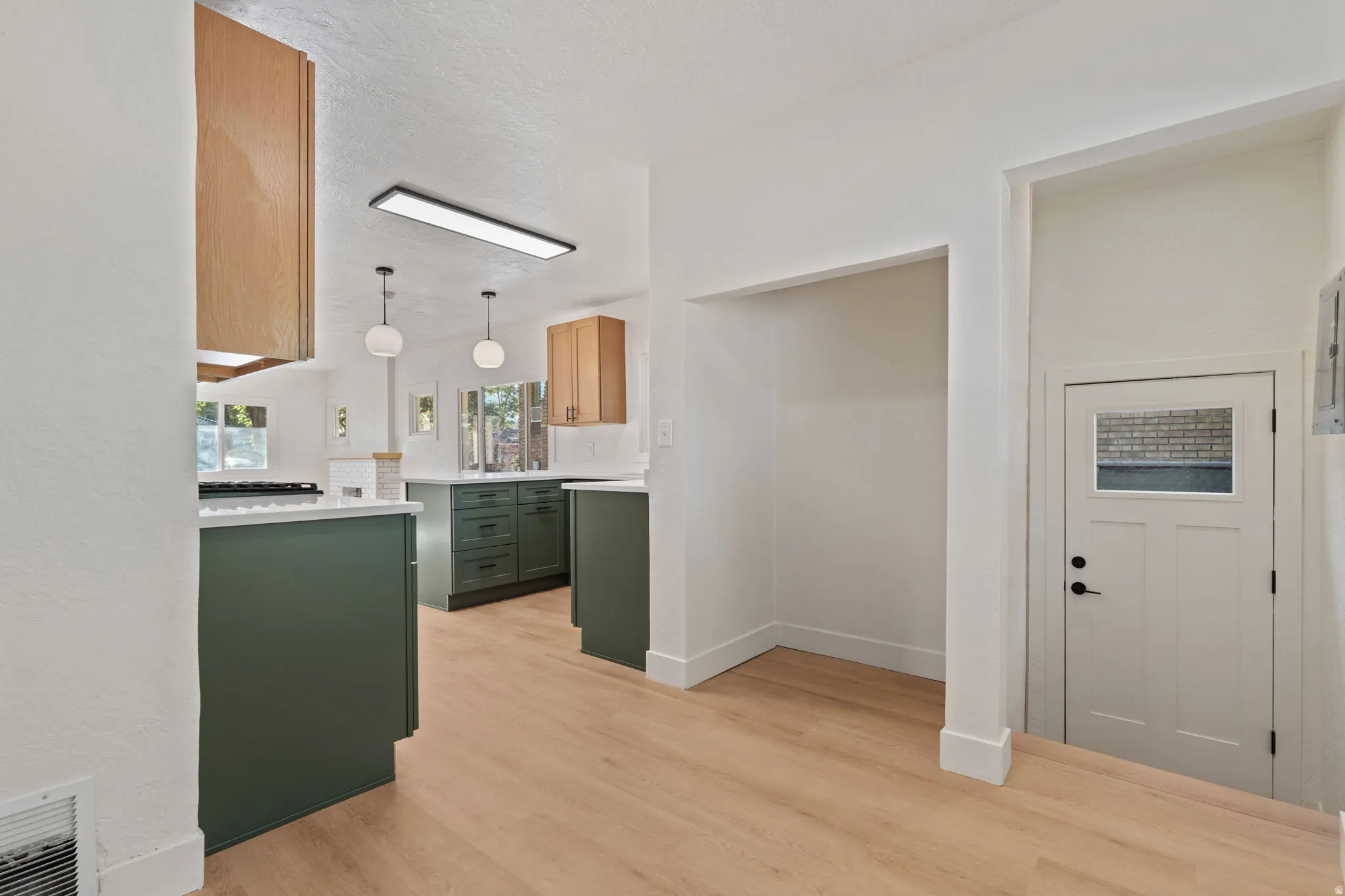 Wood-finish flooring throughout, paired with white walls, and a kitchen featuring dark green lower cabinetry and light wood-tone upper cabinetry