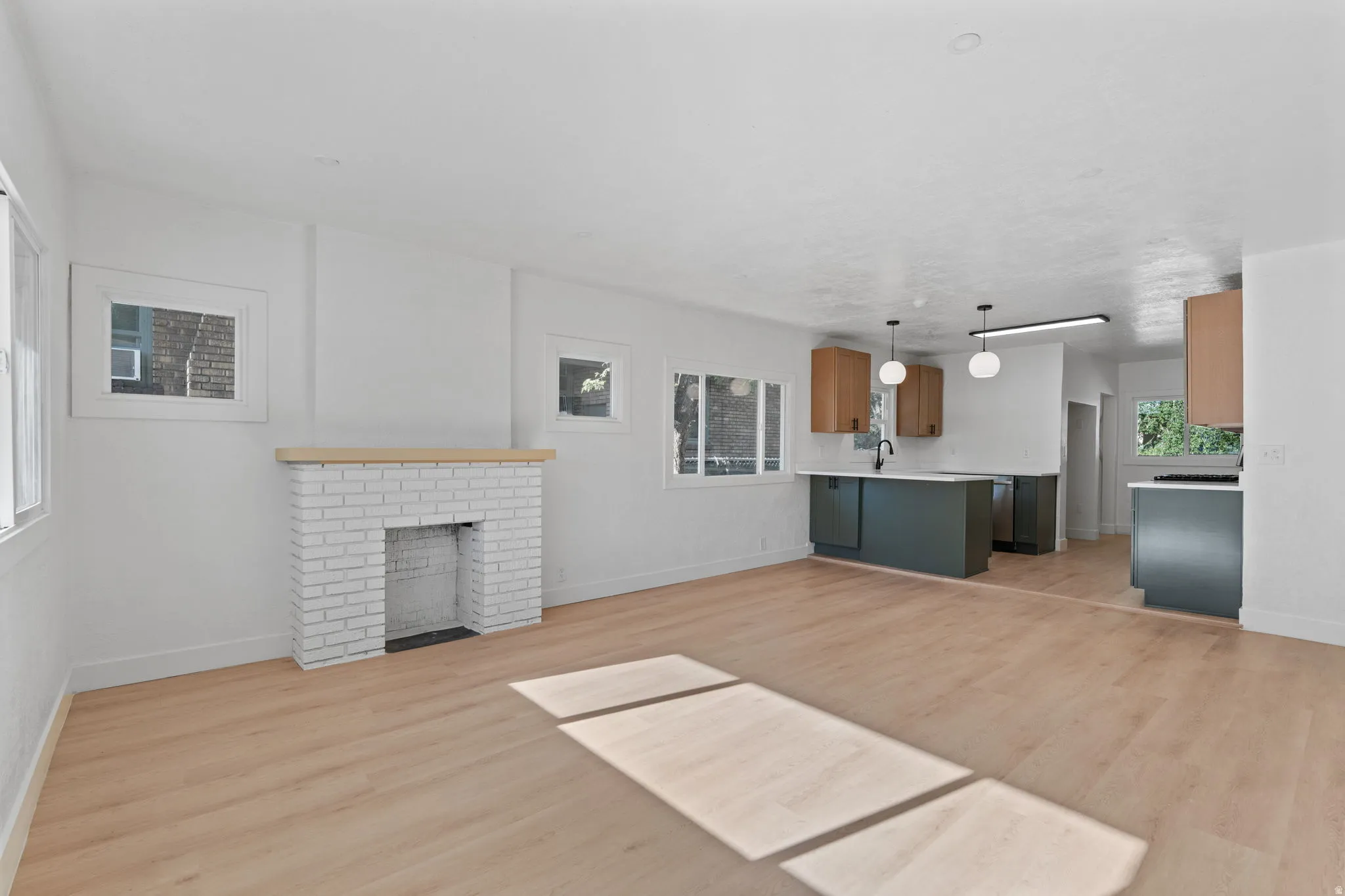 Open-concept living space featuring wood-finish flooring, a white brick fireplace with a wood mantel, and recessed lighting