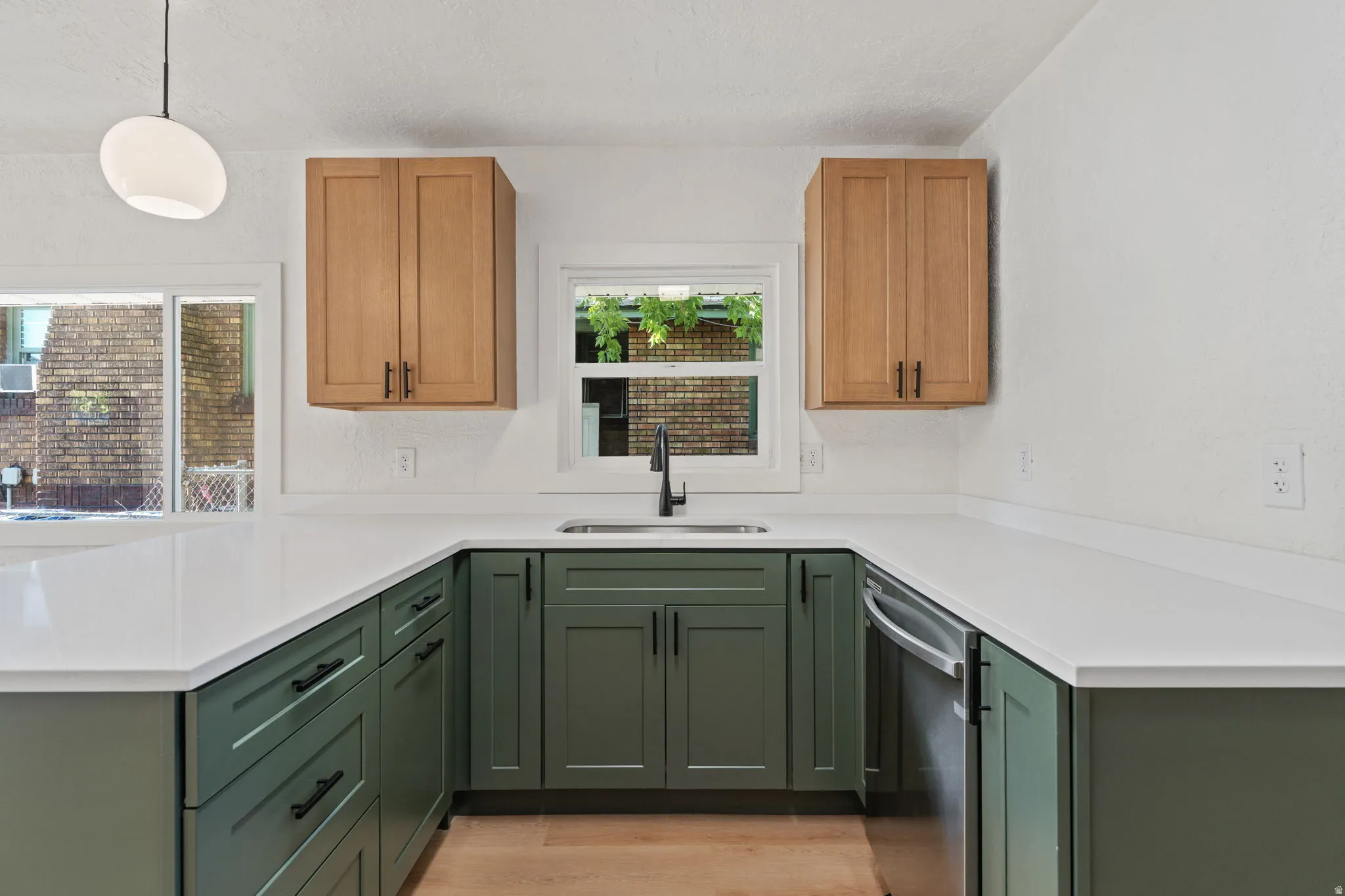 U-shaped kitchen featuring white countertops, green shaker-style lower cabinetry, and light wood-finish upper cabinetry