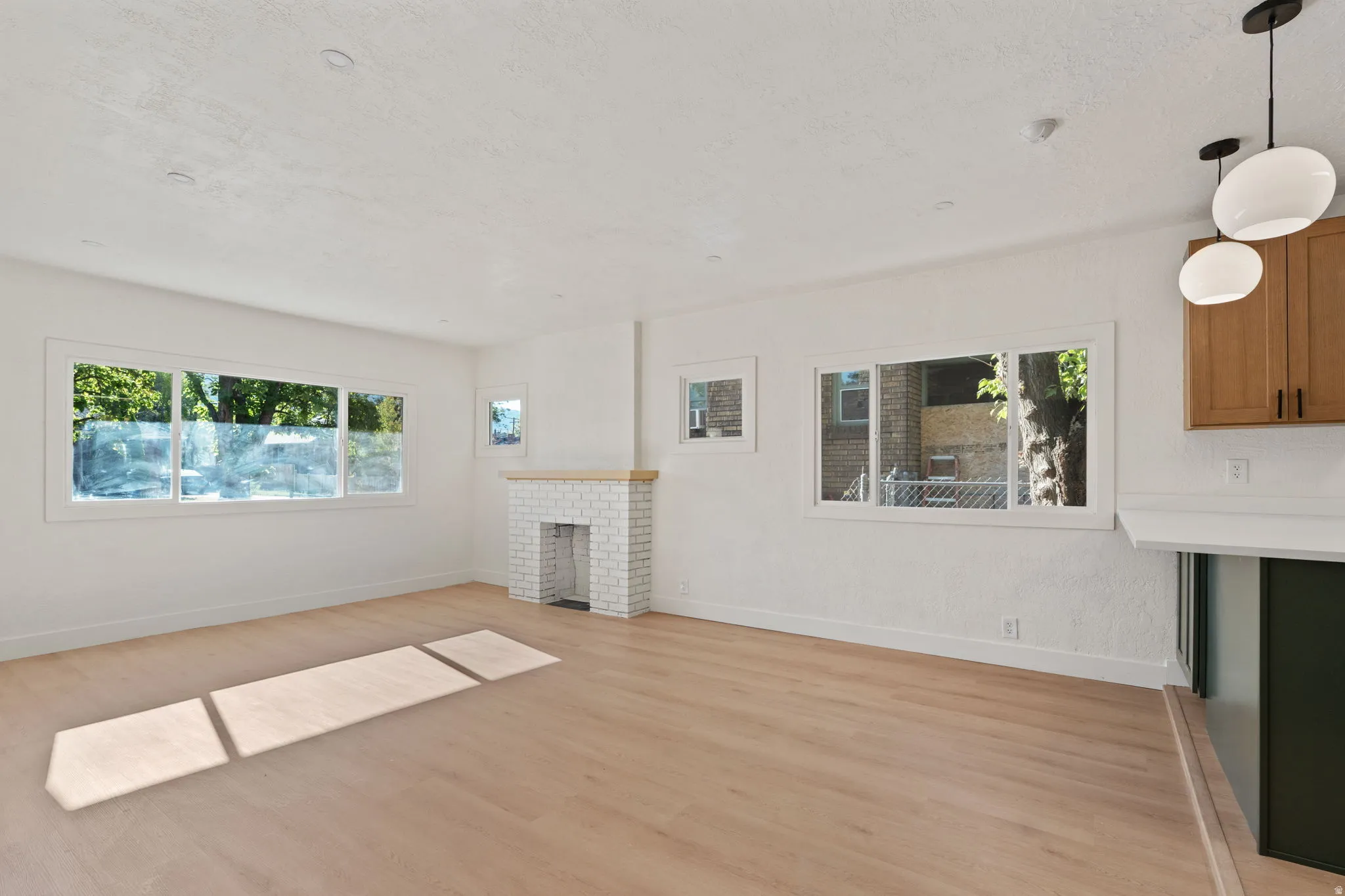 Light wood-finish flooring, white painted walls, white brick fireplace with wood mantel, white framed windows, and recessed lighting