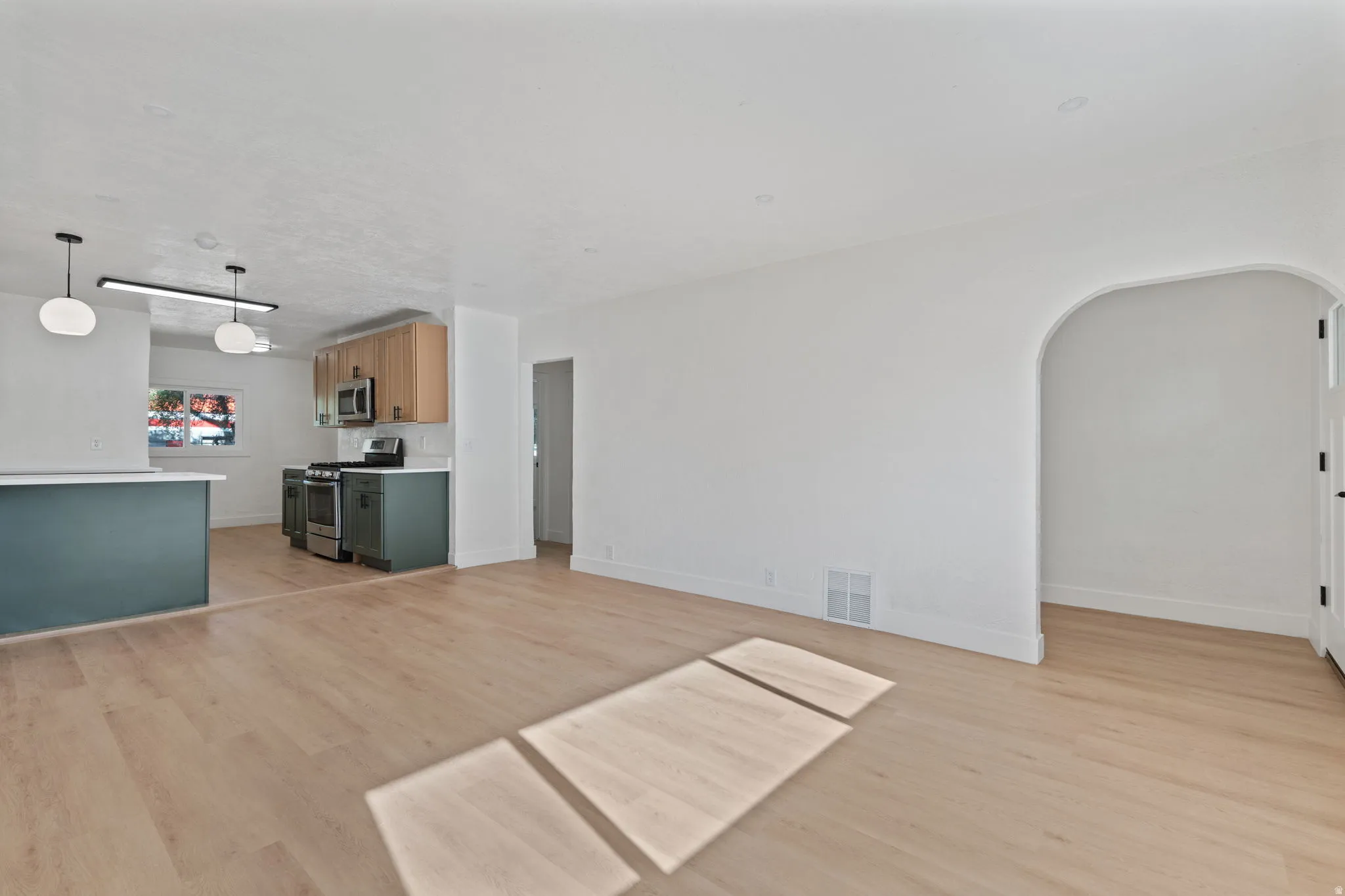 Open-concept living space featuring light wood-finish flooring, a kitchen with two-tone cabinetry, stainless steel appliances, and a curved archway