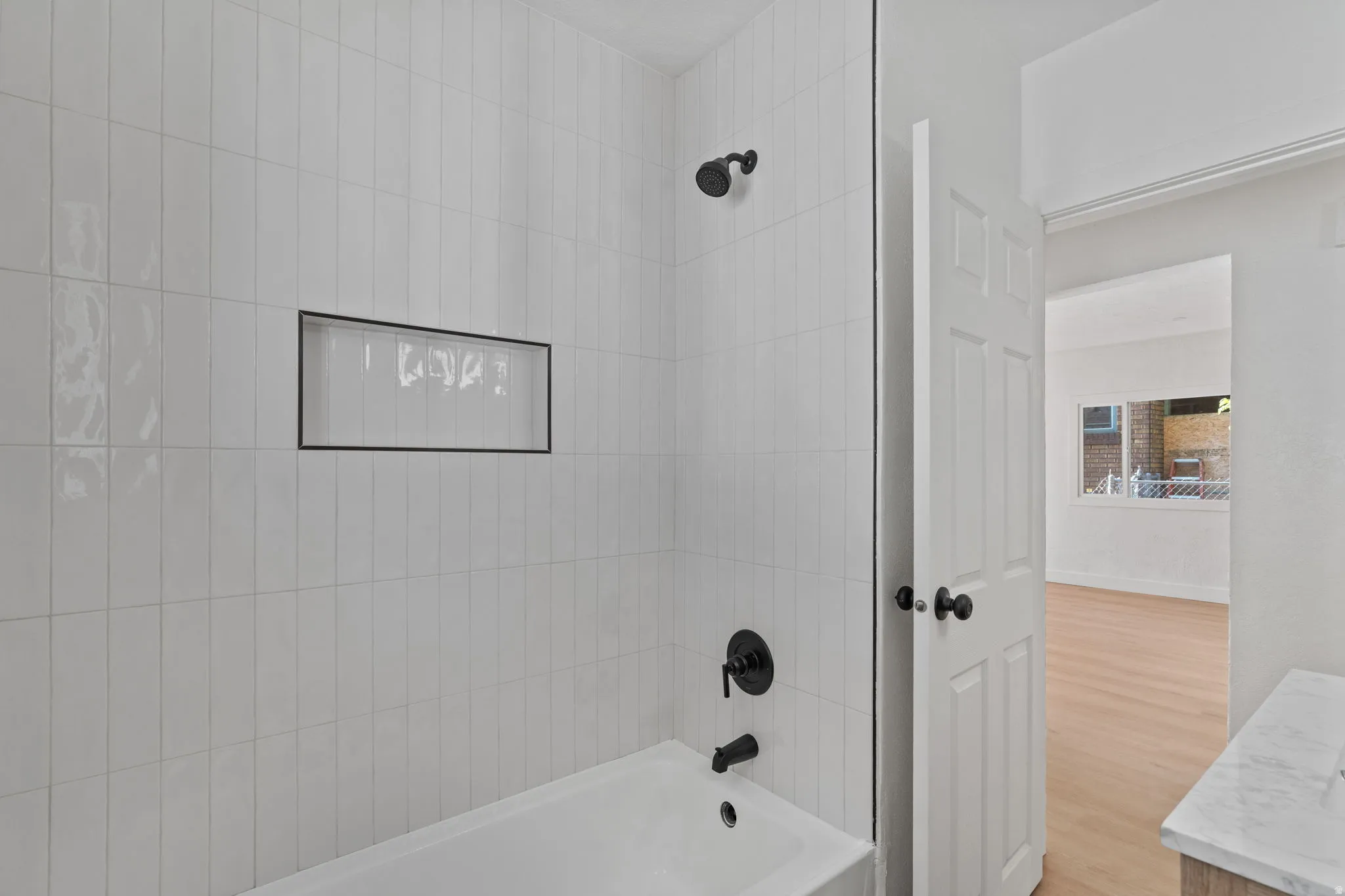 Bathtub with white subway tile surround, recessed shower niche, and matte black fixtures