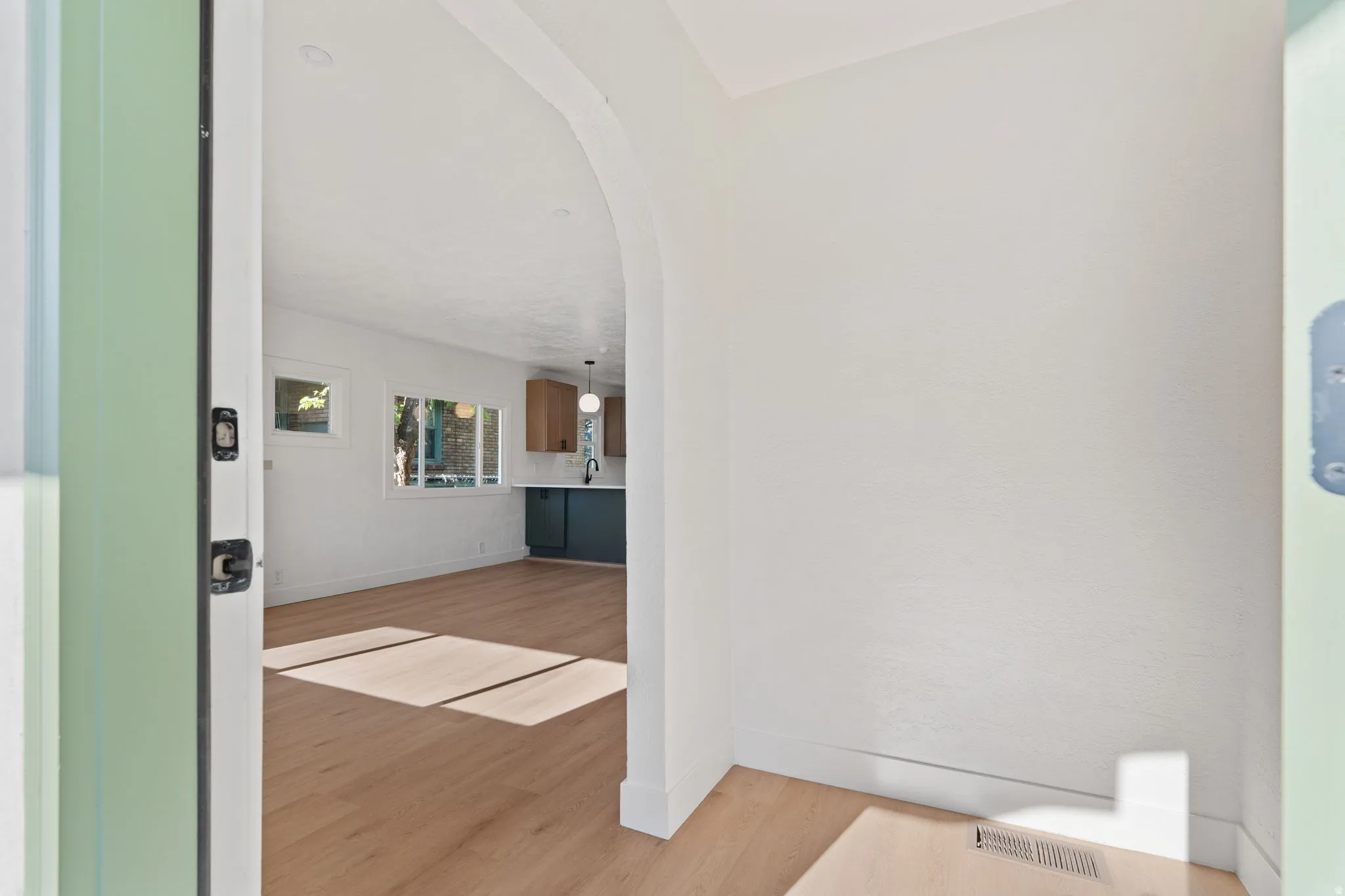 Arched entryway leading to a living area with wood-finish flooring, recessed lighting, and multiple windows