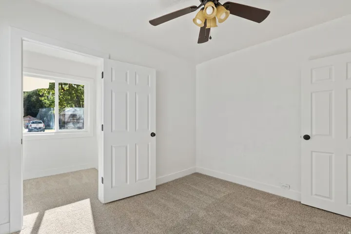 Neutral-toned carpeting, white interior doors with black hardware, and a ceiling fan with integrated lighting