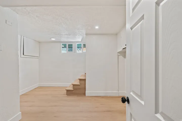 Recessed lighting, wood-finish flooring, white paneled door, black doorknob, and natural light from transom windows