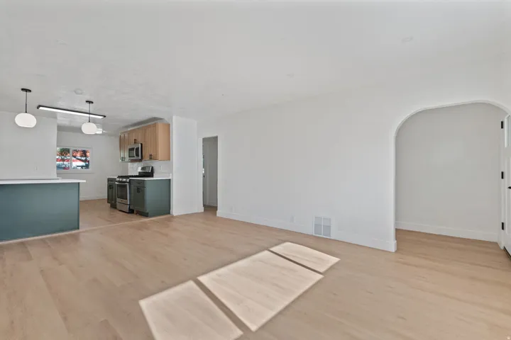 Open-concept living space featuring light wood-finish flooring, a kitchen with two-tone cabinetry, stainless steel appliances, and a curved archway