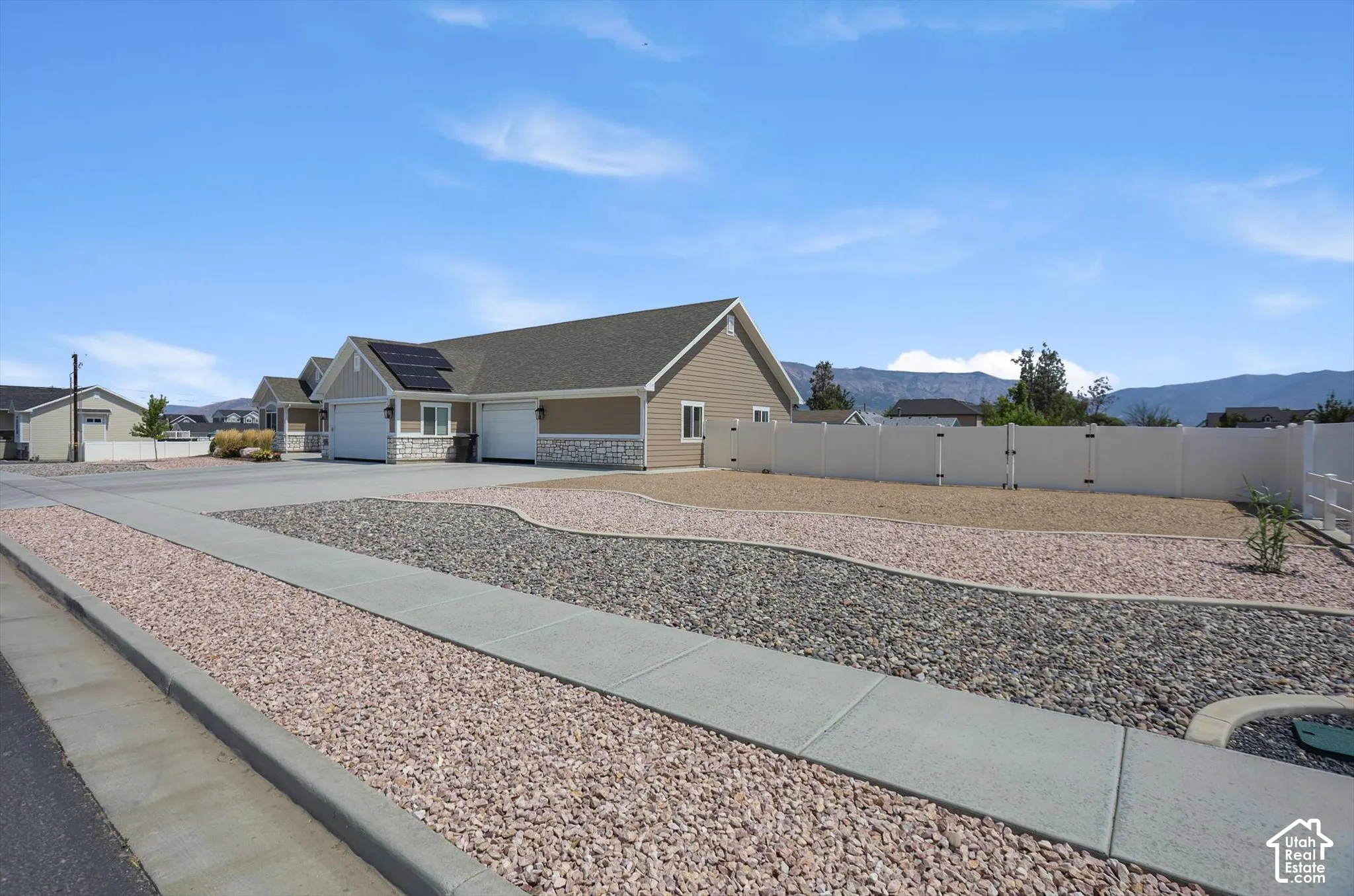 Exterior featuring a vinyl privacy fence, landscaped rock beds, a concrete driveway, attached garage, and solar panels