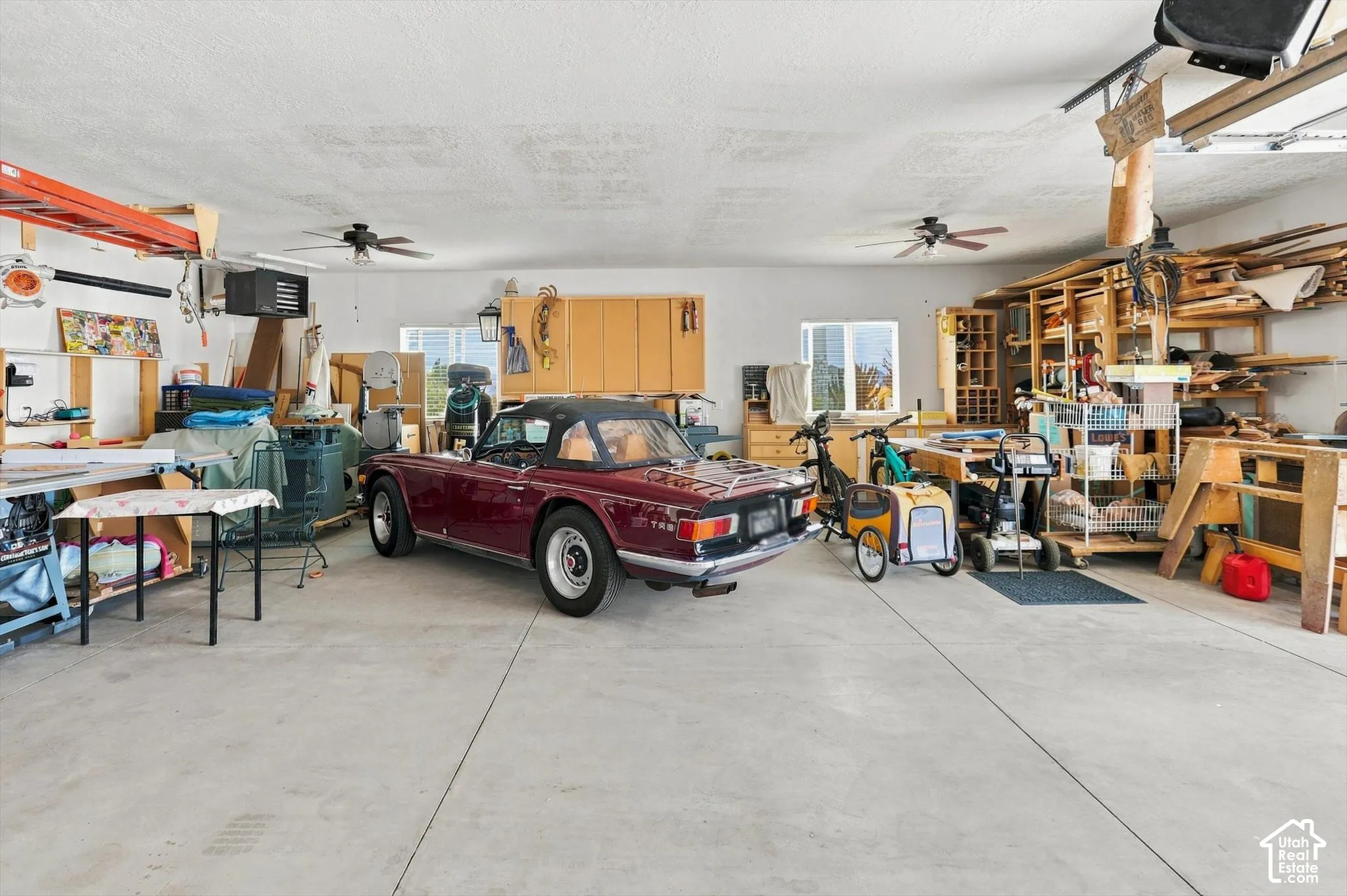 Spacious garage with concrete flooring, multiple windows, built-in shelving, and installed ceiling fans