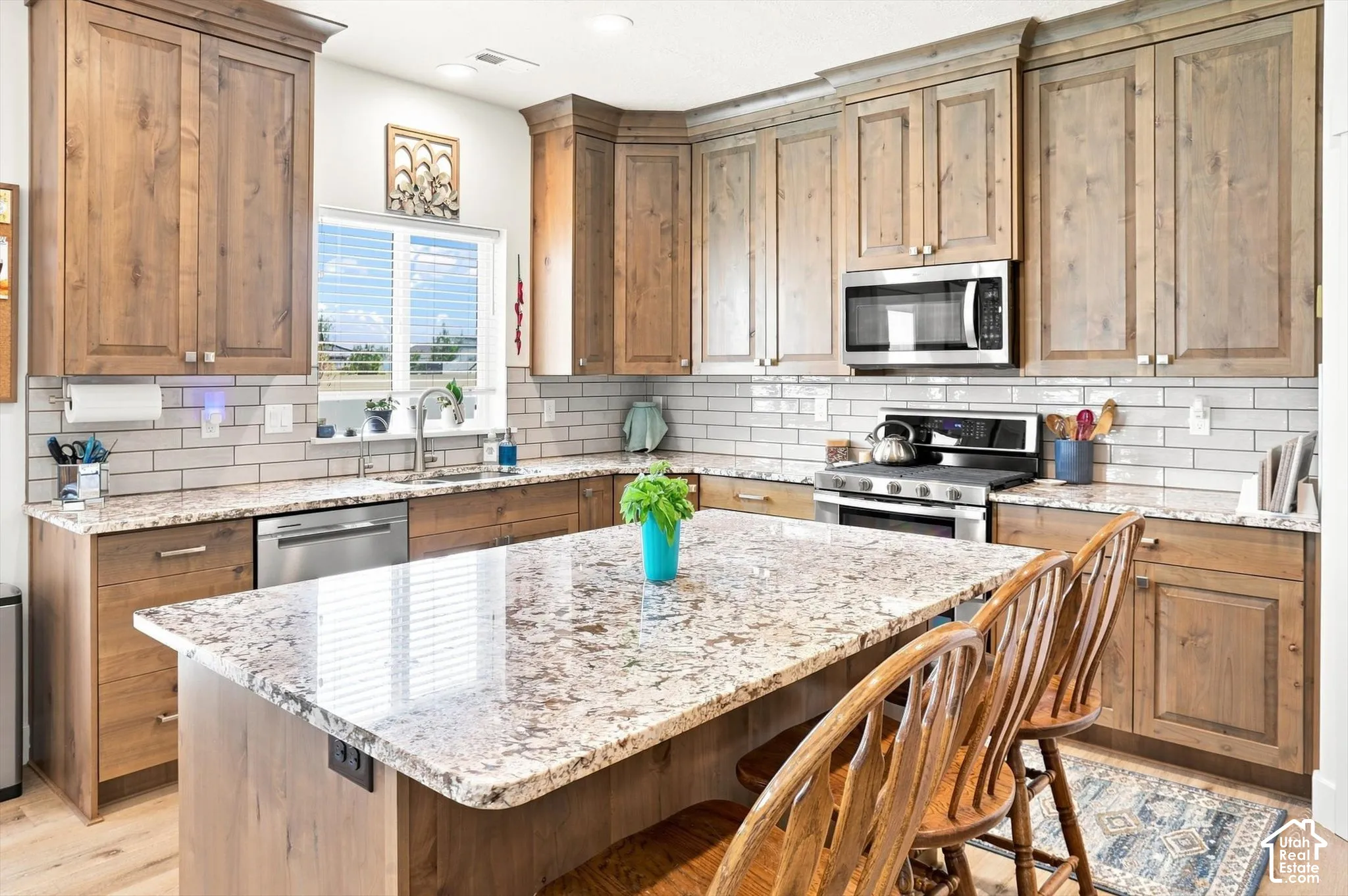 Spacious kitchen featuring wood-finish cabinetry, granite countertops, a large island with seating, a subway tile backsplash, and stainless steel appliances