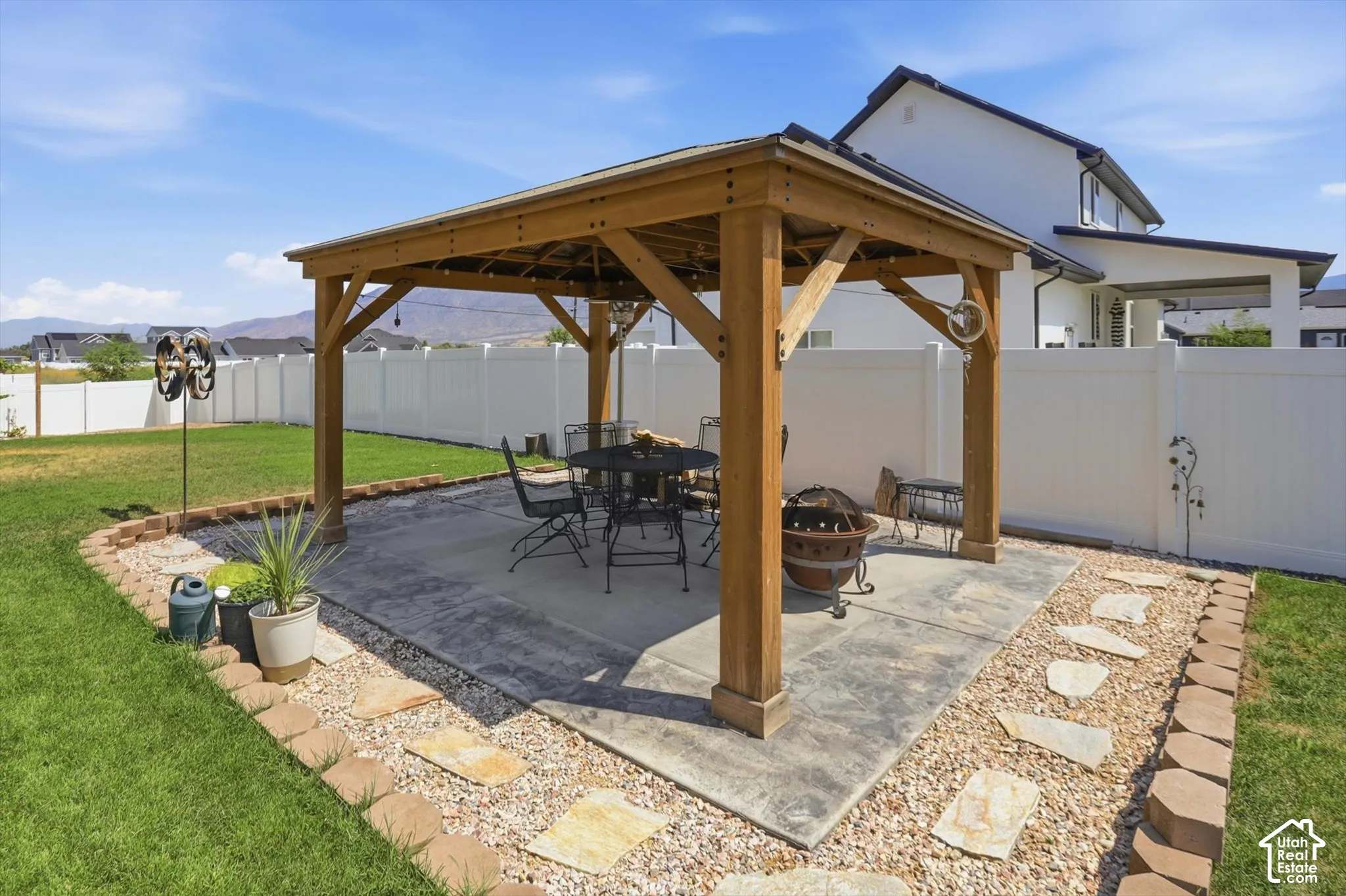 Backyard featuring a wooden pergola over a concrete patio, a gravel border with stepping stones, and a surrounding white privacy fence