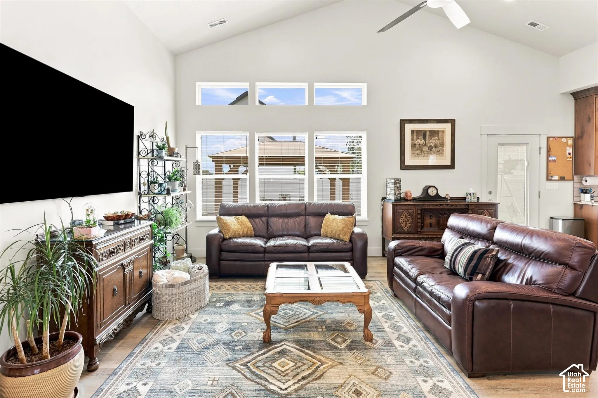 Vaulted ceiling with a ceiling fan, multiple windows, wood-finish flooring, and white walls