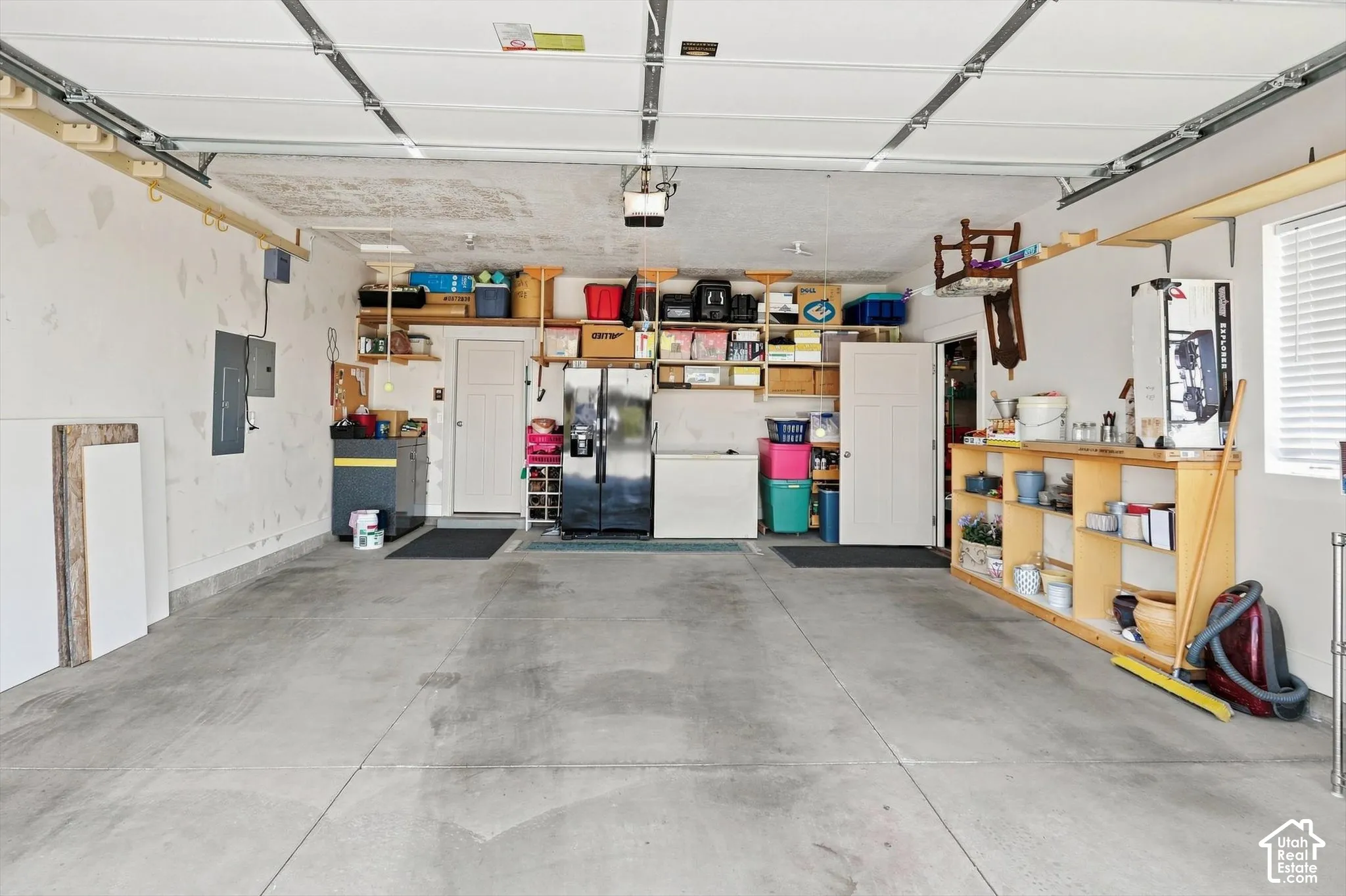 Concrete flooring, overhead garage door system, exposed ceiling joists, built-in shelving, and white walls