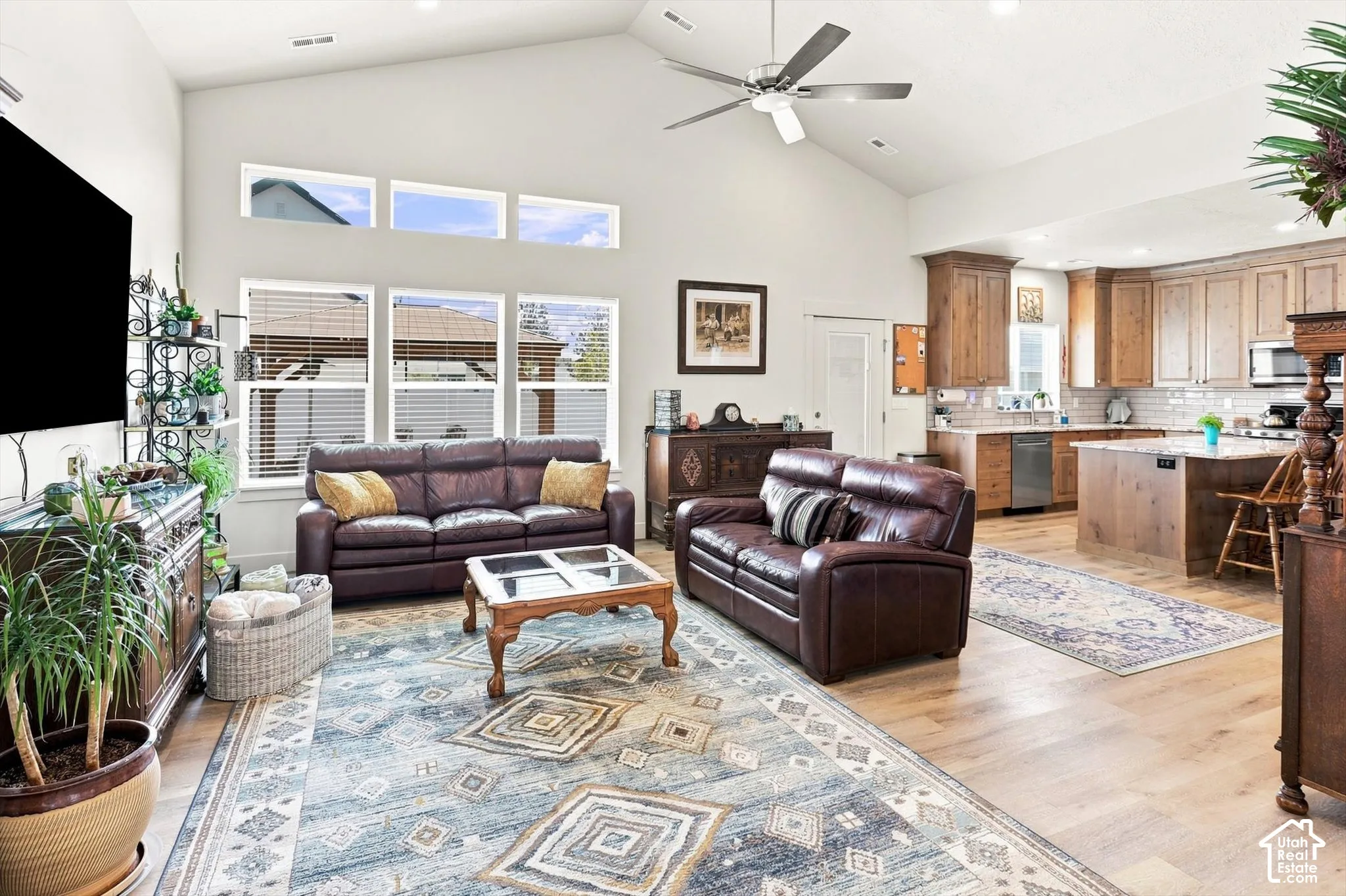 Vaulted ceilings with a ceiling fan, light wood-finish flooring, a kitchen featuring wood cabinetry, a tile backsplash, and an island with a countertop