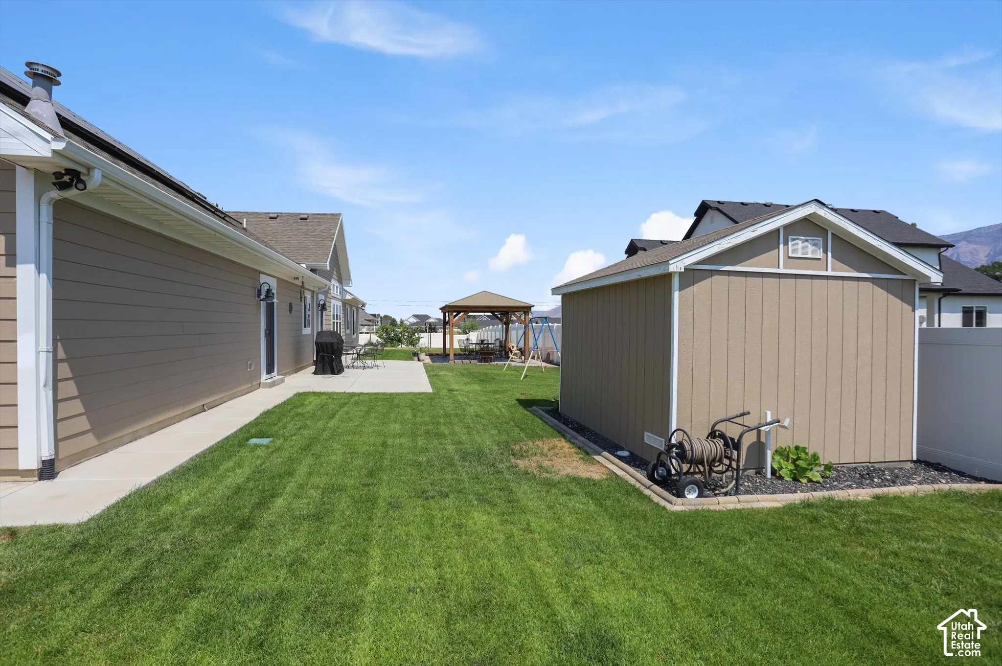 Expansive lawn area featuring a concrete patio, a detached storage shed, and a privacy fence