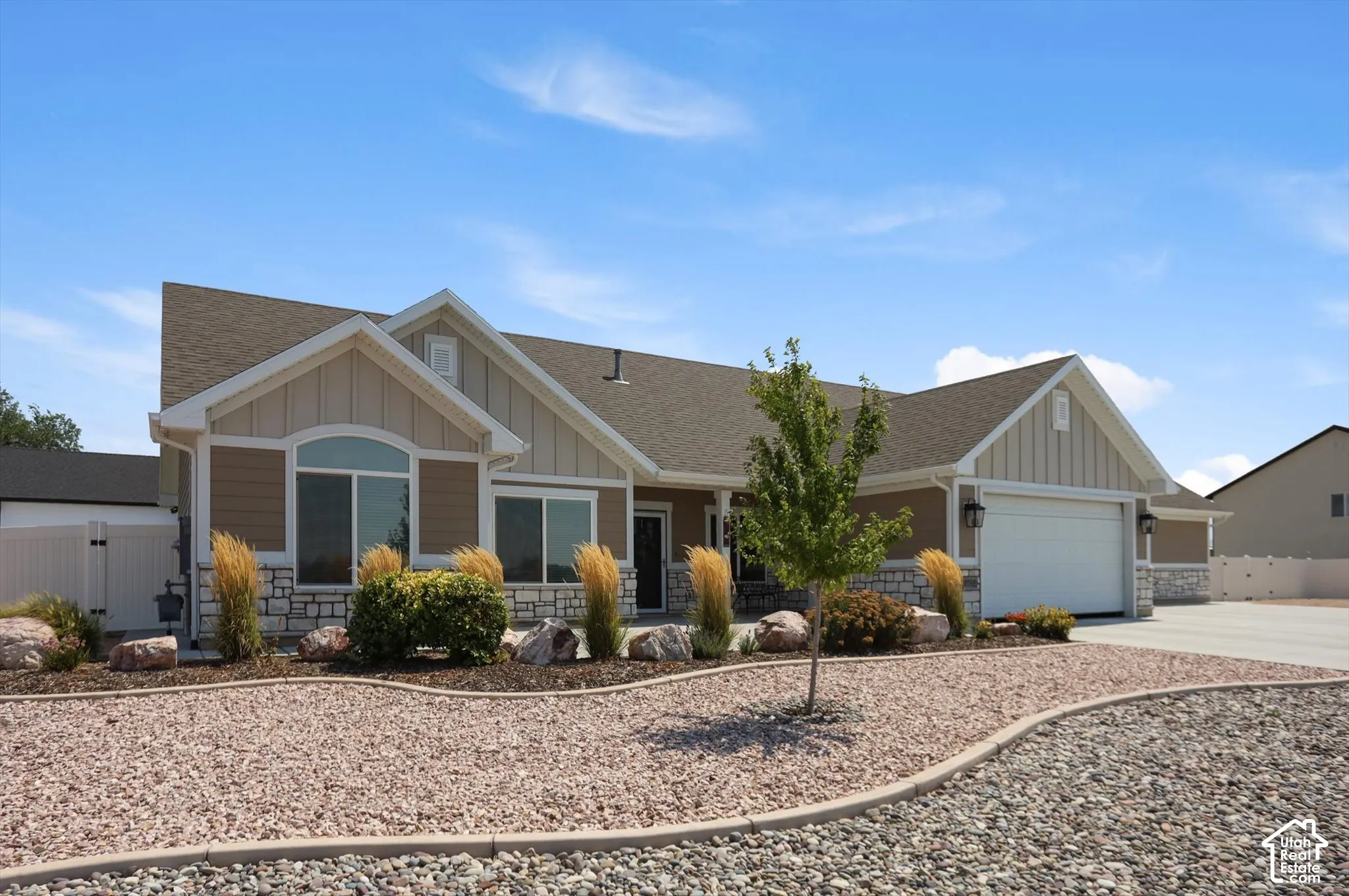 Exterior featuring a light tan and white facade, stone detailing, a prominent two-car garage, and a low-maintenance gravel and rock landscape