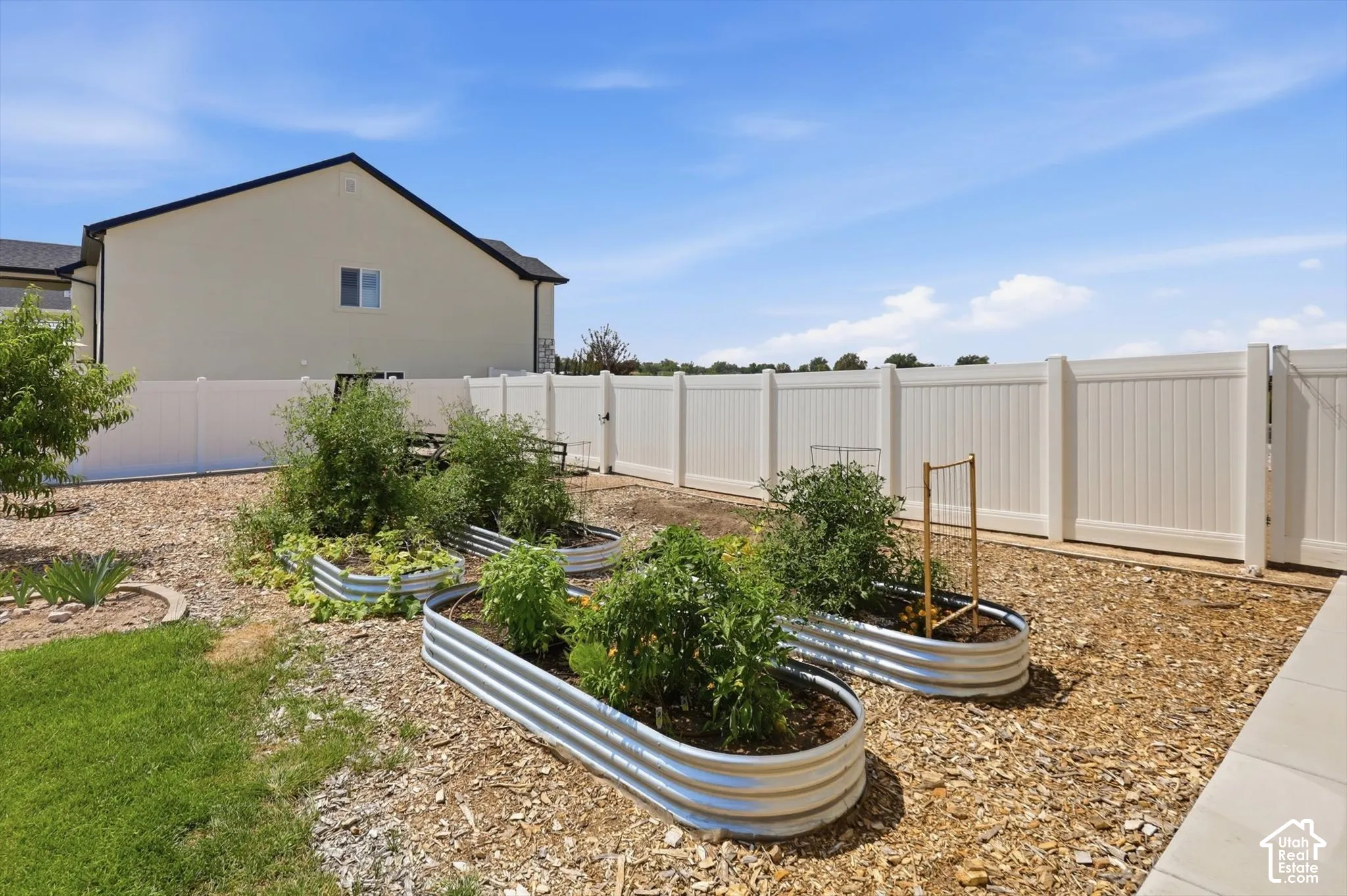 Manicured backyard with a privacy fence, raised garden beds, and a paved patio area