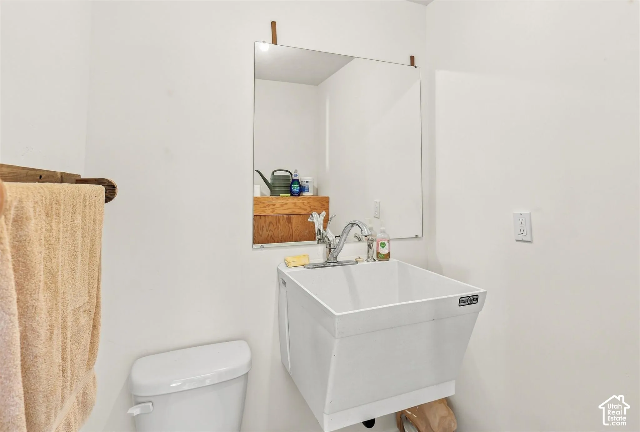 White utility sink with chrome faucet, wall-mounted mirror, and white toilet