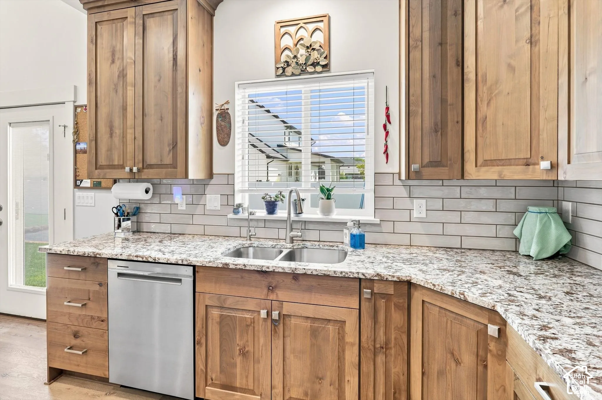 Wood-finish cabinetry, speckled countertops, subway tile backsplash, and a stainless steel dishwasher