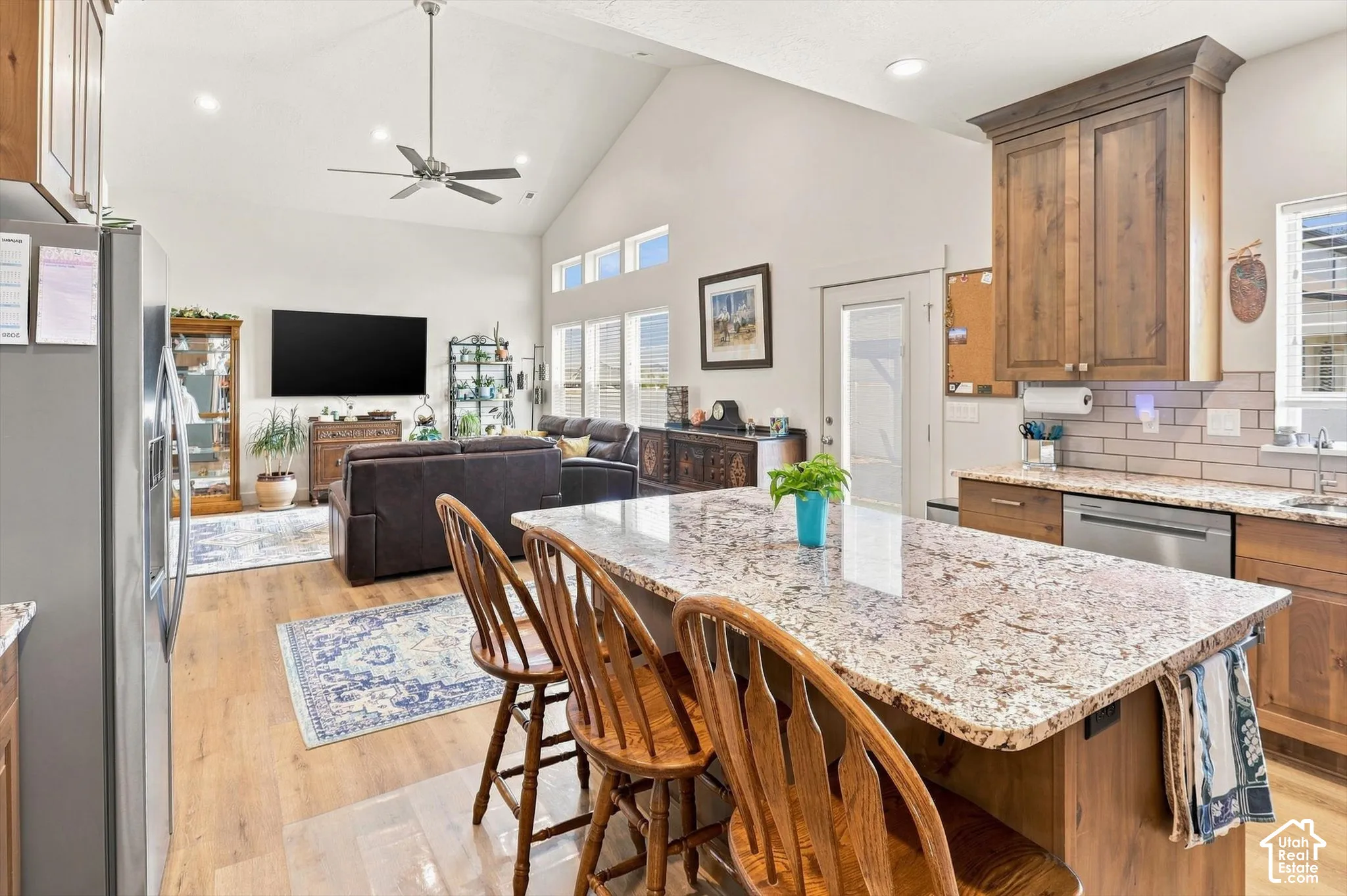 Vaulted ceiling with a ceiling fan, wood-finish flooring, kitchen island with a stone countertop, subway tile backsplash, and stainless steel appliances