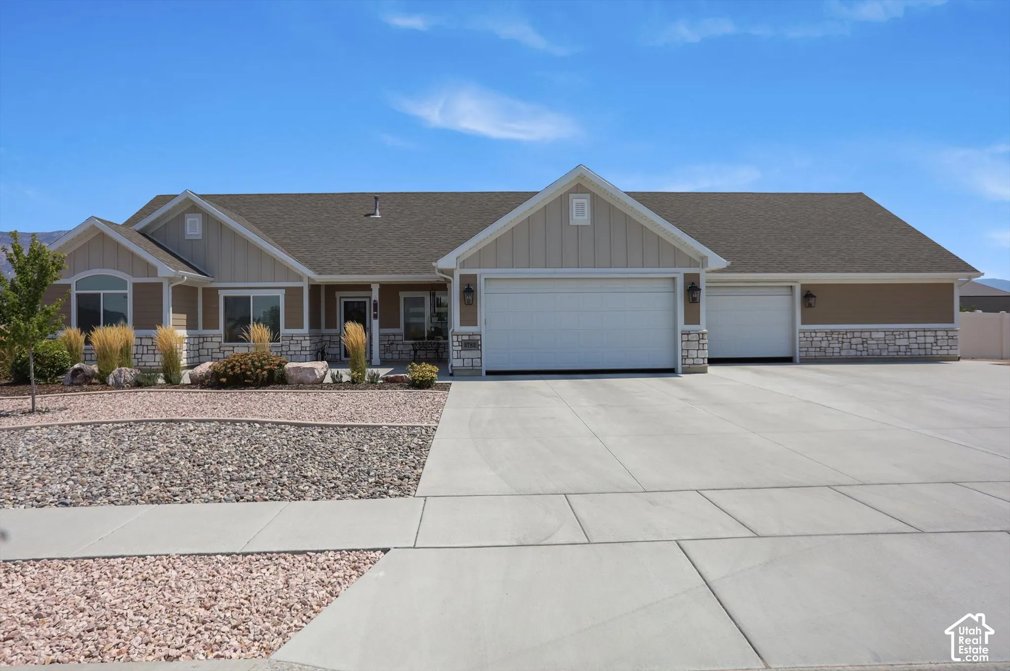 Large concrete driveway, attached three-car garage, stone and siding exterior, xeriscaped front yard, and covered entry