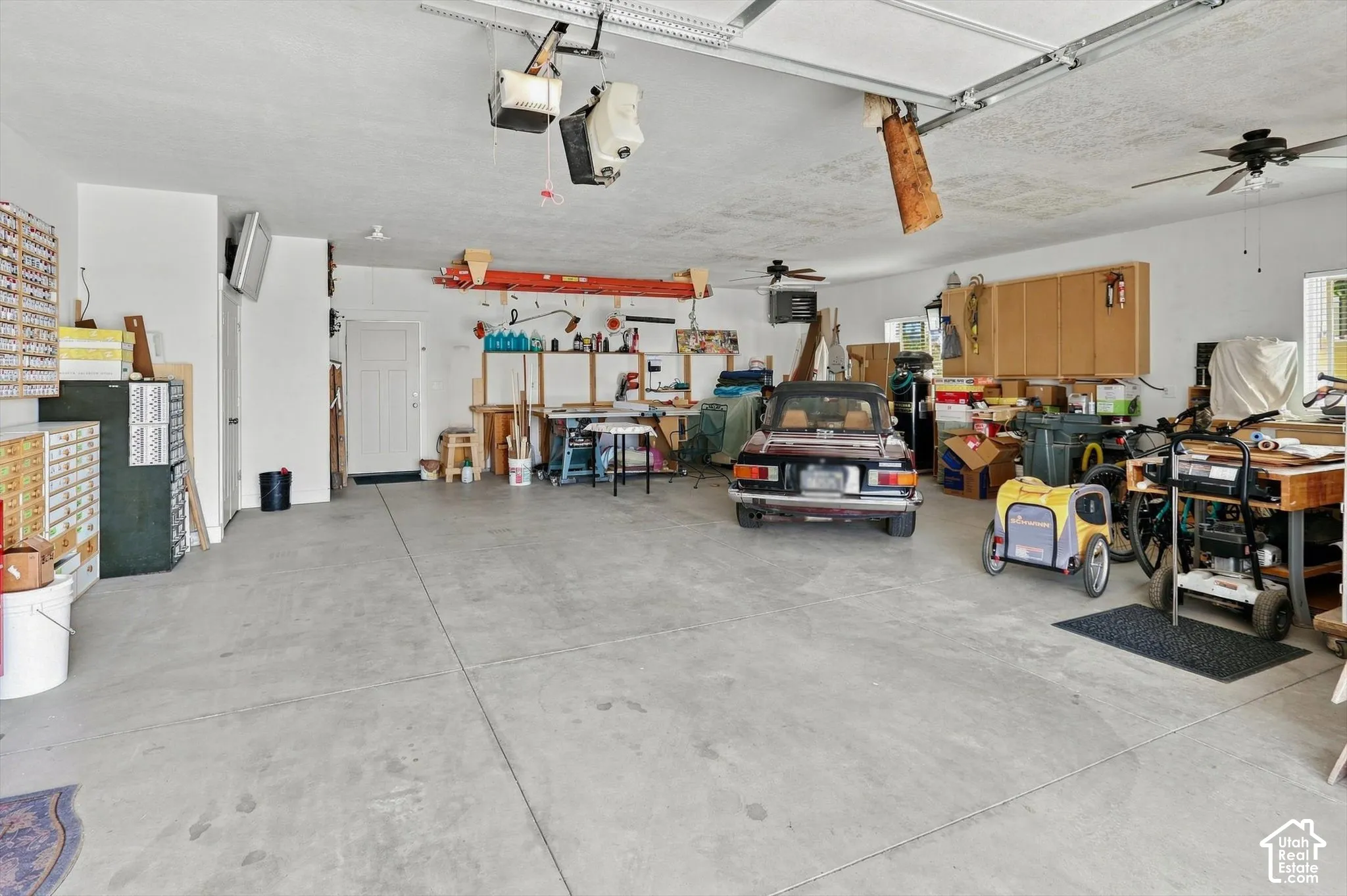 Spacious garage featuring concrete flooring, overhead garage door system, wall-mounted cabinetry, and dual ceiling fans