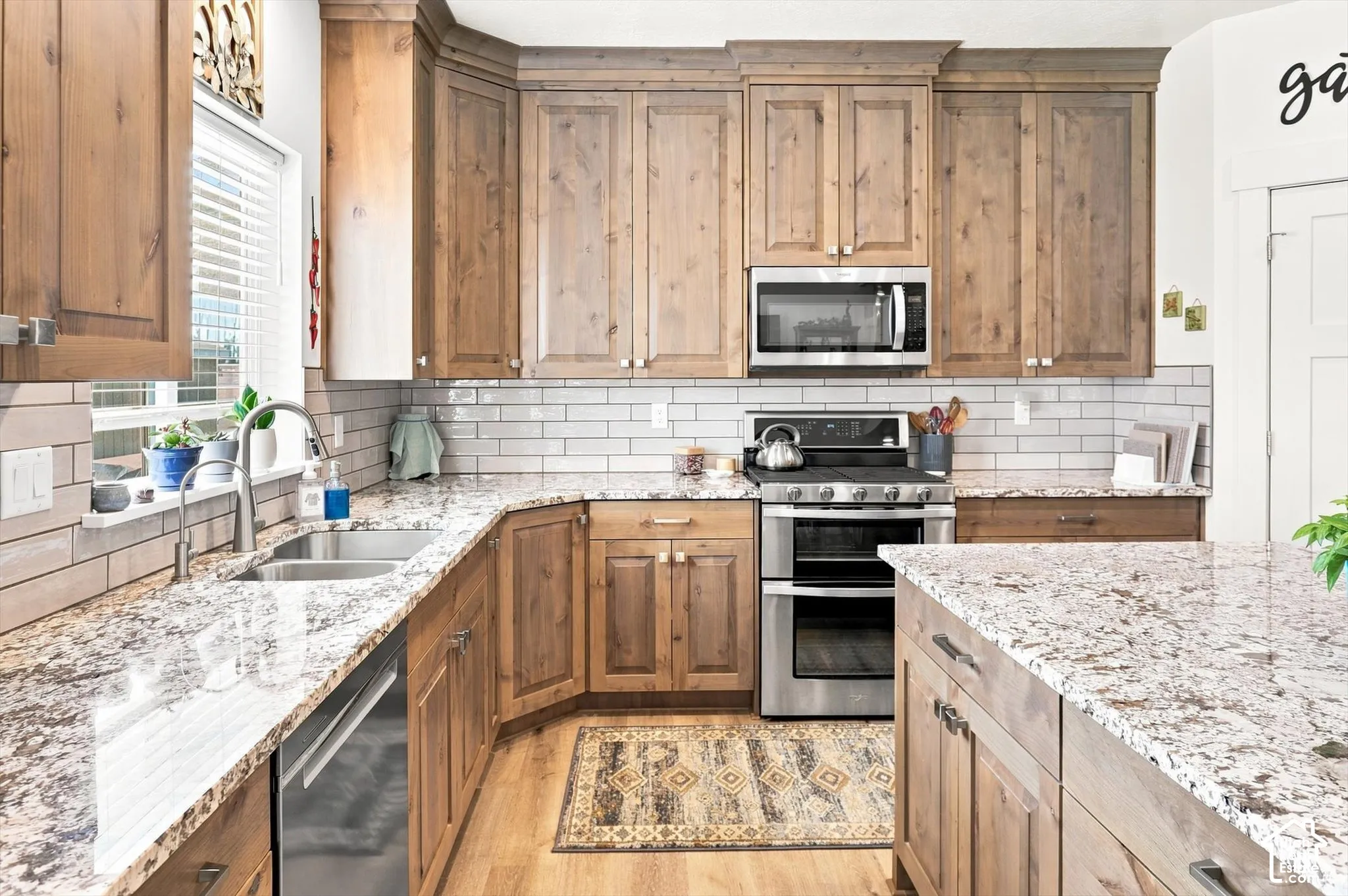 Kitchen featuring wood cabinetry, stainless steel appliances, a double basin sink, light-toned countertops, and a subway tile backsplash