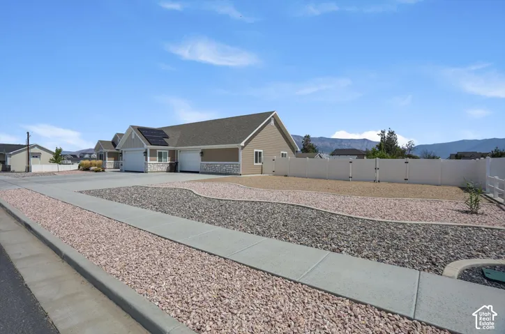 Exterior featuring a vinyl privacy fence, landscaped rock beds, a concrete driveway, attached garage, and solar panels