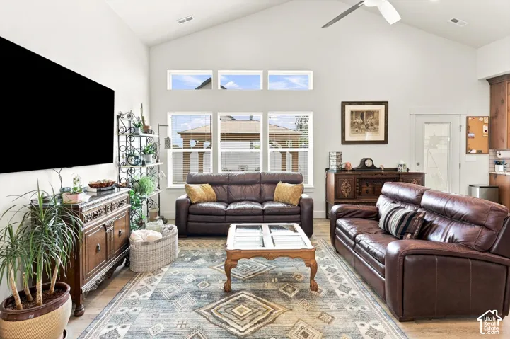 Vaulted ceiling with a ceiling fan, multiple windows, wood-finish flooring, and white walls
