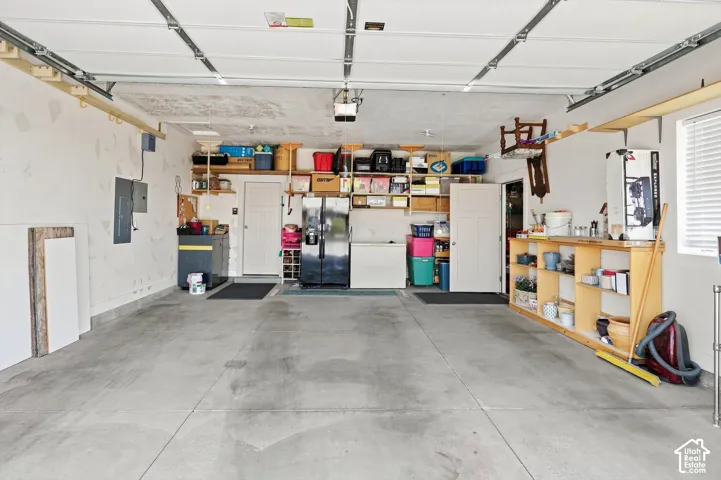 Concrete flooring, overhead garage door system, exposed ceiling joists, built-in shelving, and white walls