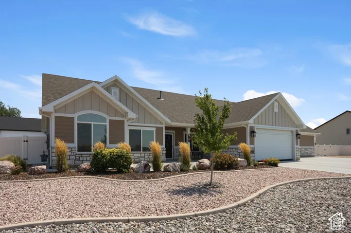 Exterior featuring a light tan and white facade, stone detailing, a prominent two-car garage, and a low-maintenance gravel and rock landscape